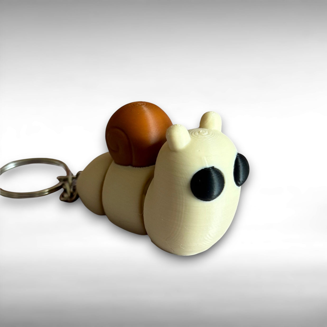 3D printed beige and brown snail-shaped keychain on a white background