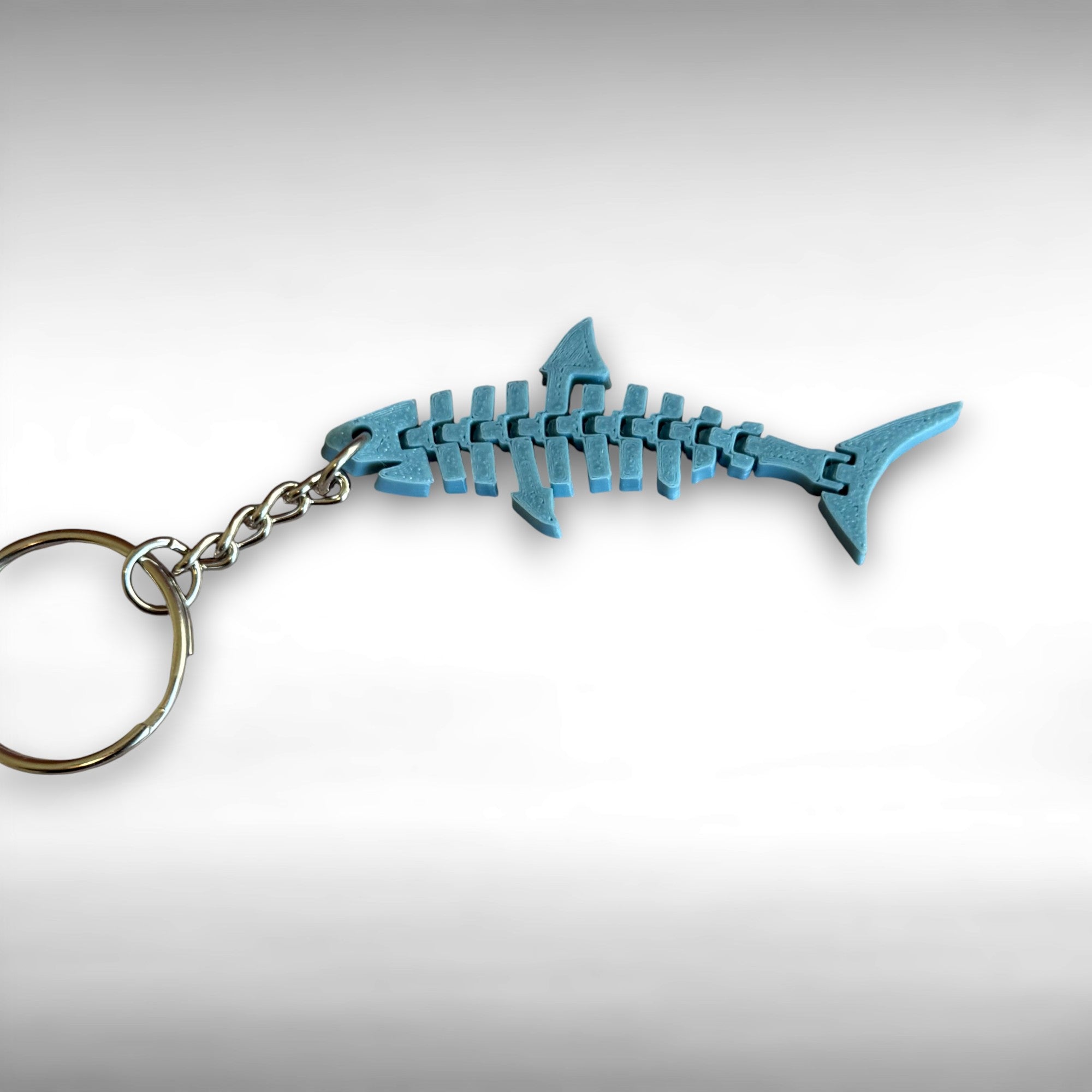3D printed blue, flat, articulated shark keychain against a white background