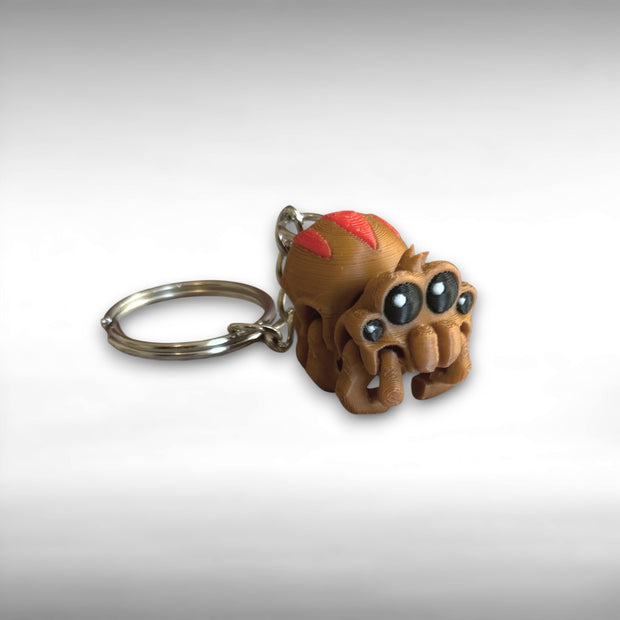 3D printed brown and red tarantula-shaped keychain with legs curled under against a light gray background