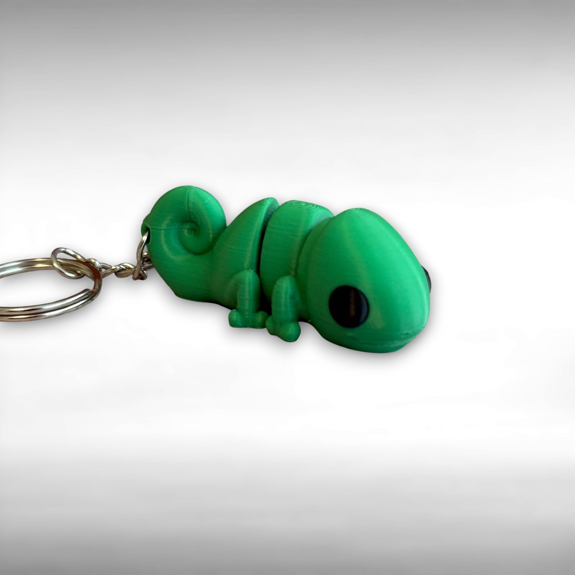 3D printed green chameleon-shaped keychain on a light gray background