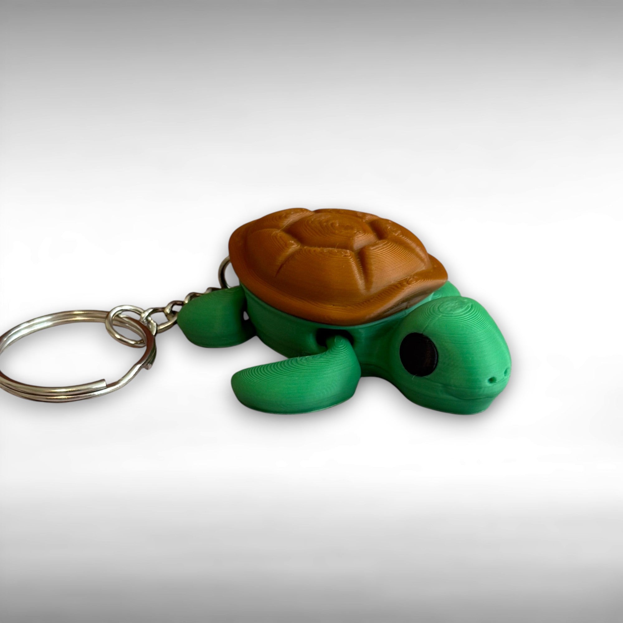 3D printed turtle-shaped keychain with brown shell and green body on a white background