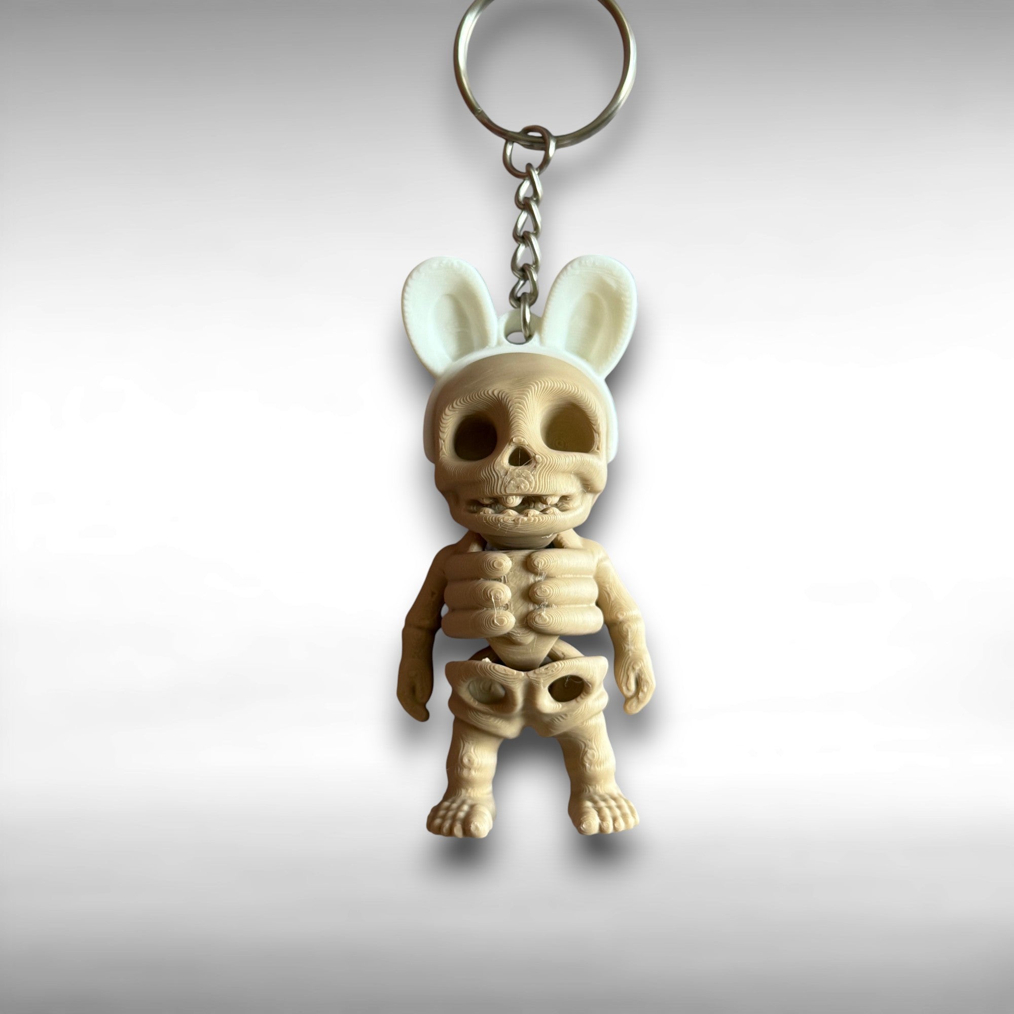 3D printed keychain of a beige skeleton with white bunny ears against a white background