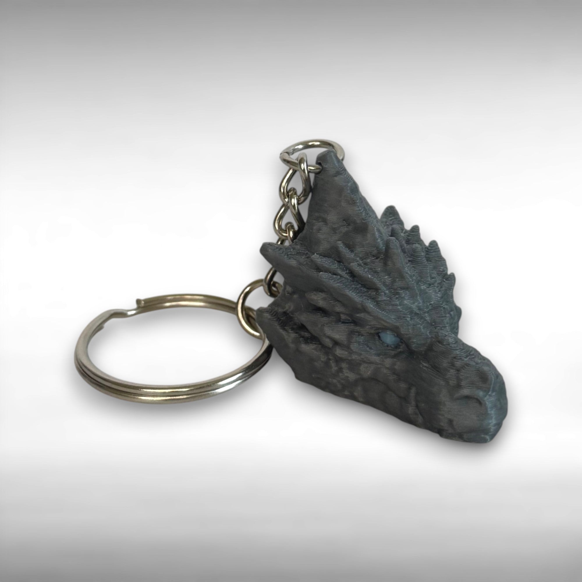 3D printed gray dragon head keychain with blue eyes on a light gray background