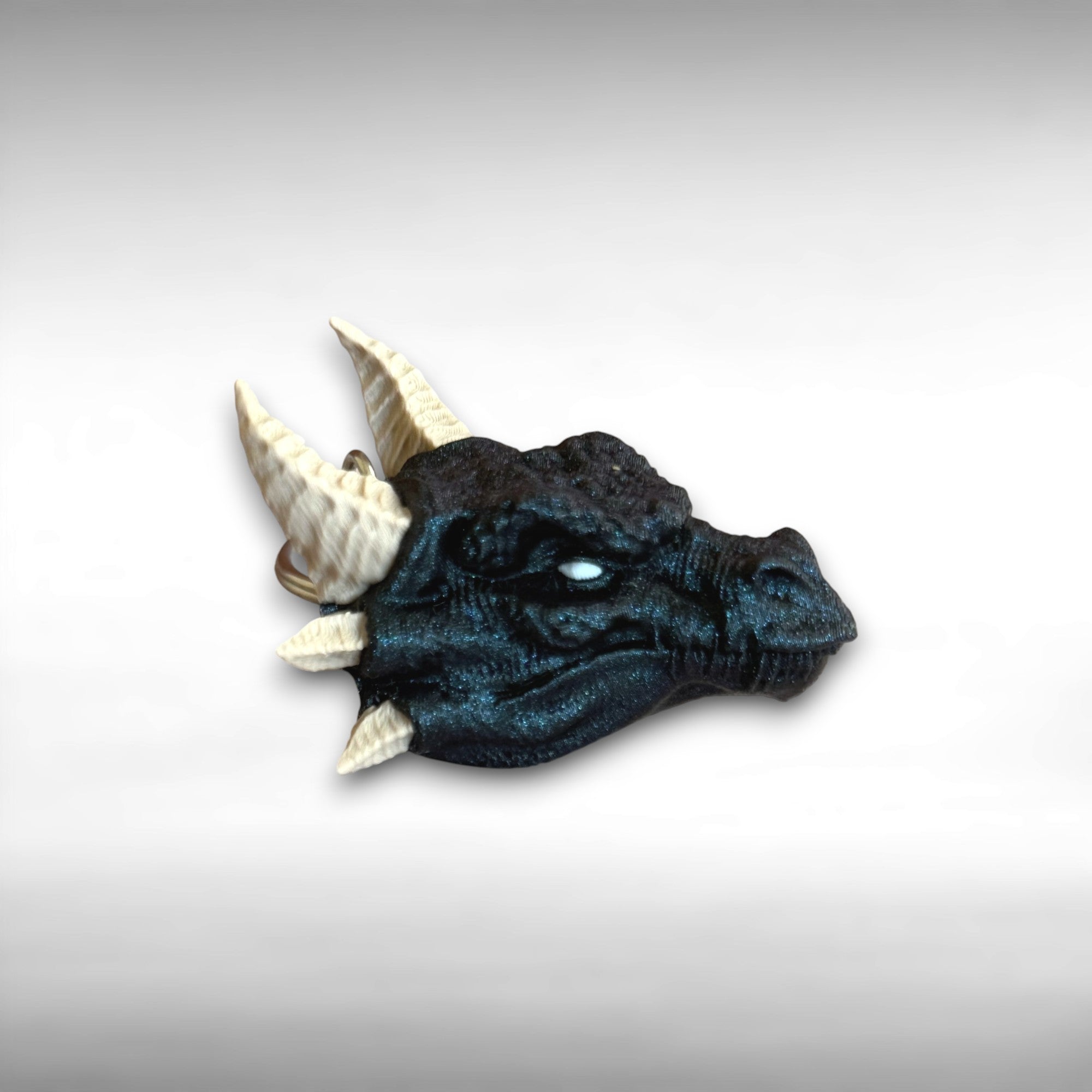 3D printed blue dragon head keychain with beige horns on a light gray background