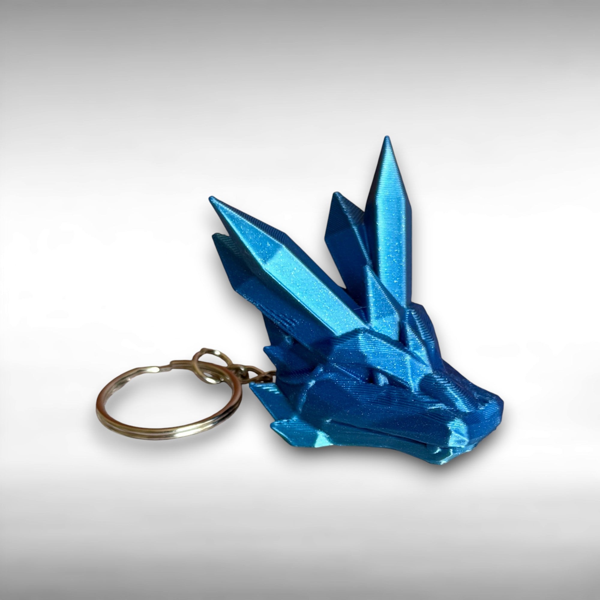 blue 3D printed keychain shaped like a dragon head with crystal-like details, against a white background