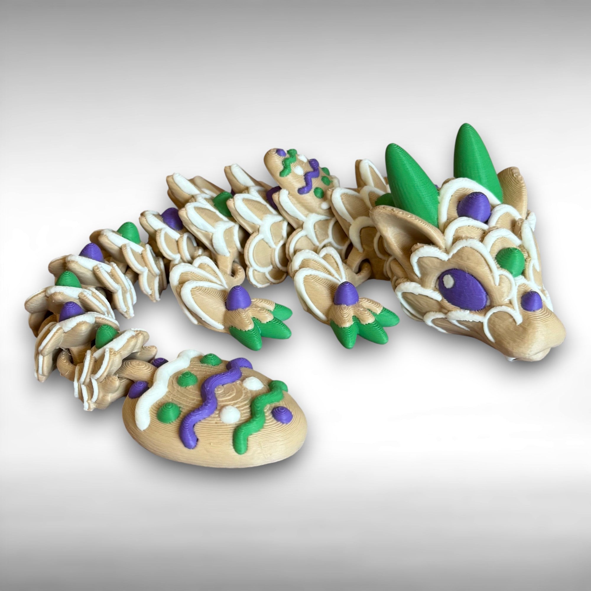3D printed beige, green, white, green, and purple cookie-shaped dragon on a white background