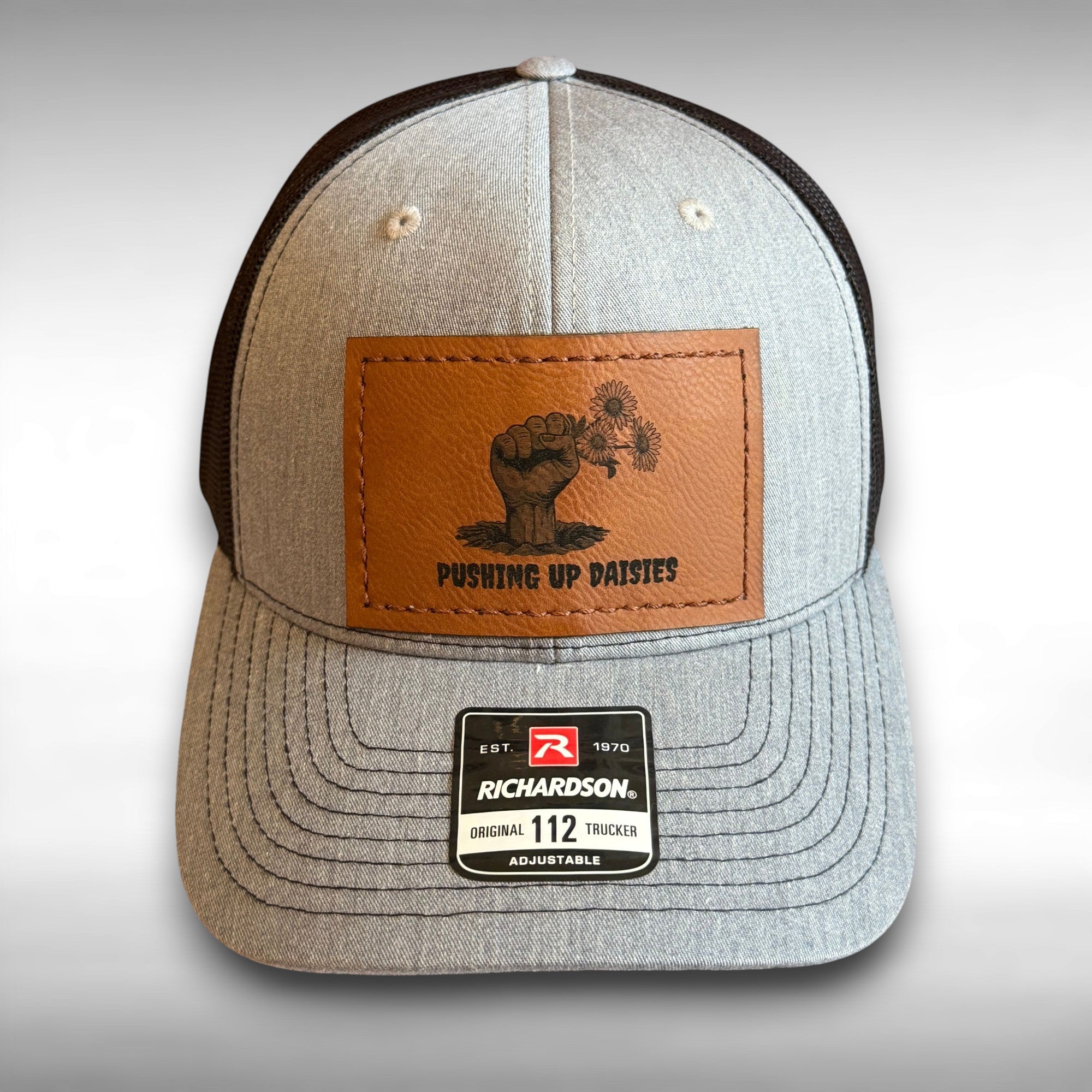 Gray and black snapback hat with rectangular leather patch featuring a zombie hand holding flowers with the phrase 