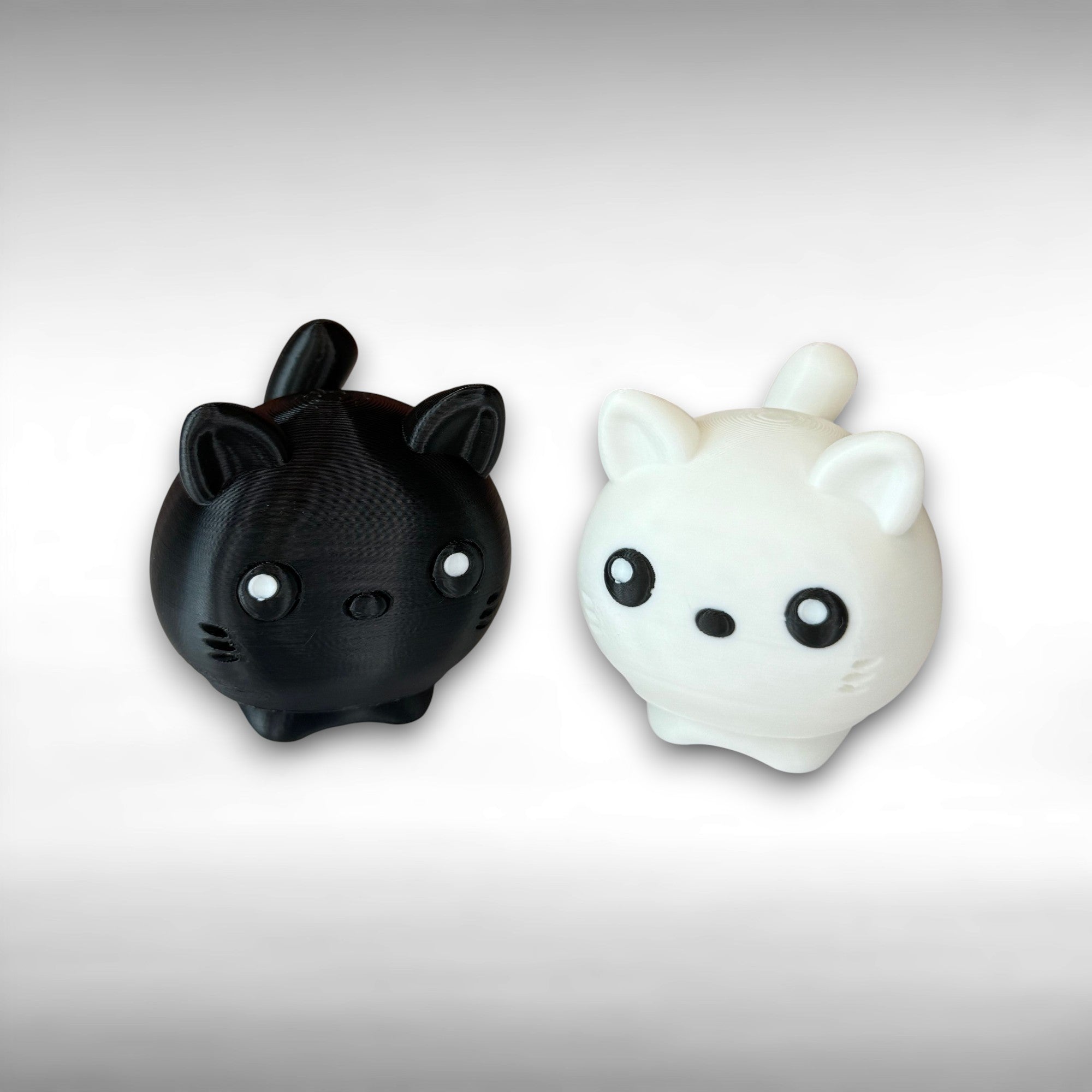 2 cat-shaped 3D printed figures, one black and one white, on a light gray background