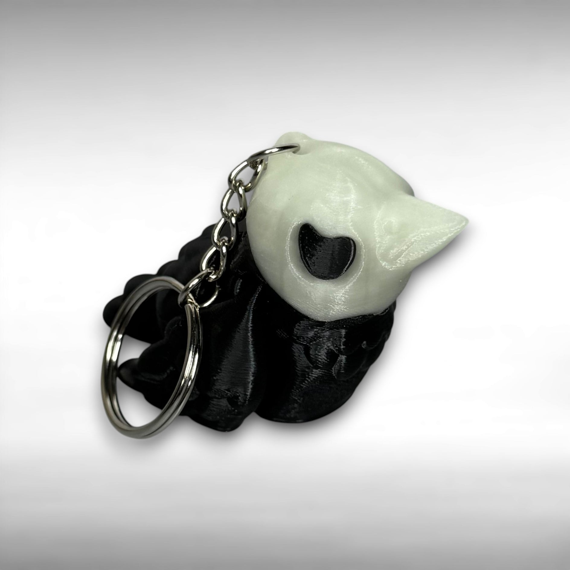 Black and white crow-shaped keychain with crow-shaped skull head on light gray background