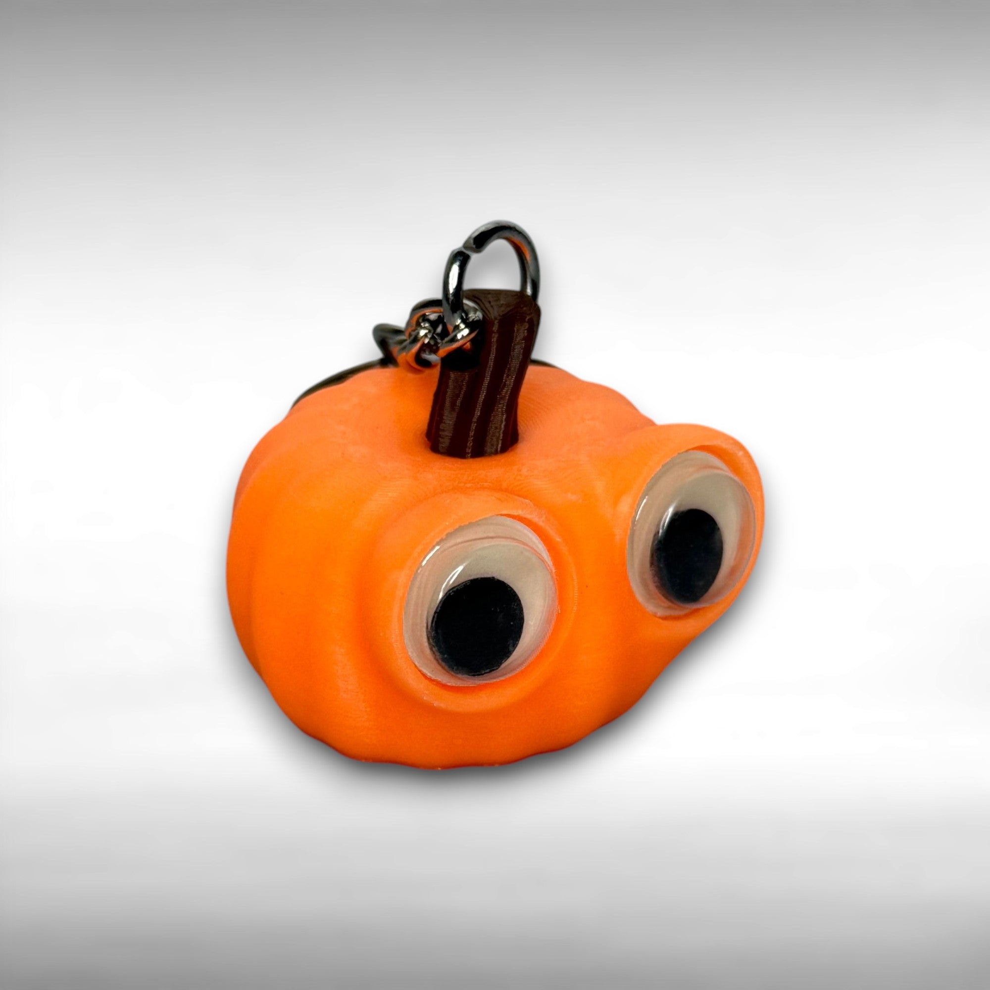 Orange pumpkin-shaped keychain with googly eyes on a gray background