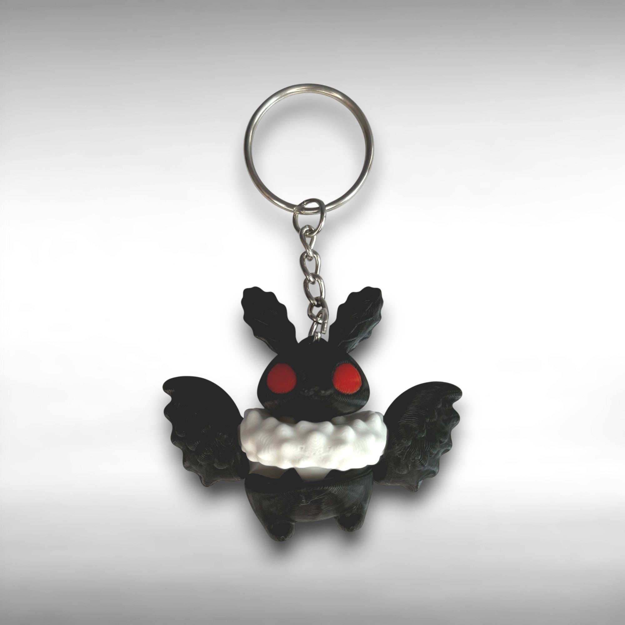 Black and white character with wings keychain with red eyes on a gray background