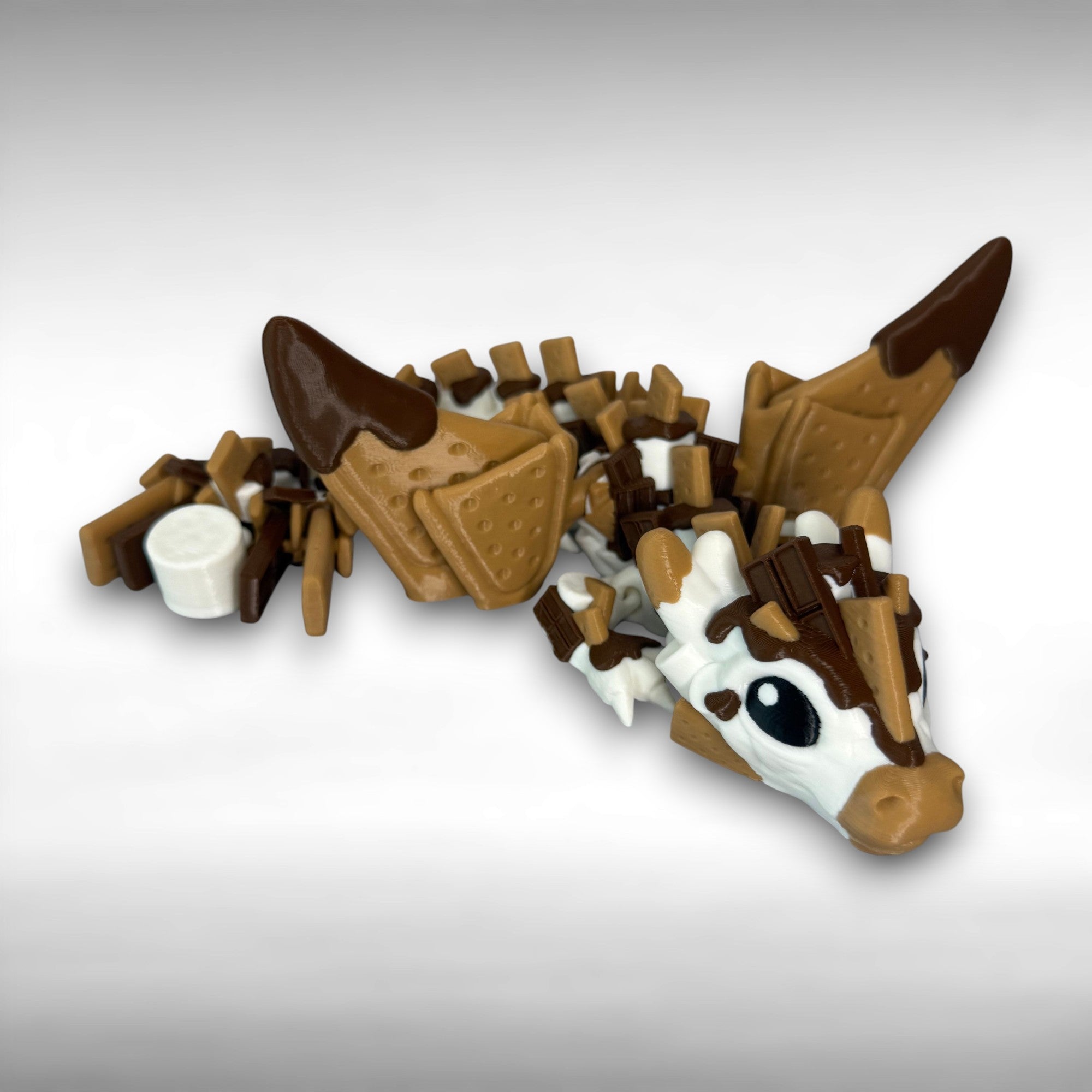 Toy figure of a dragon with a white, brown, and tan body shaped liked marshmallows, chocolate, and graham crackers on a gray background