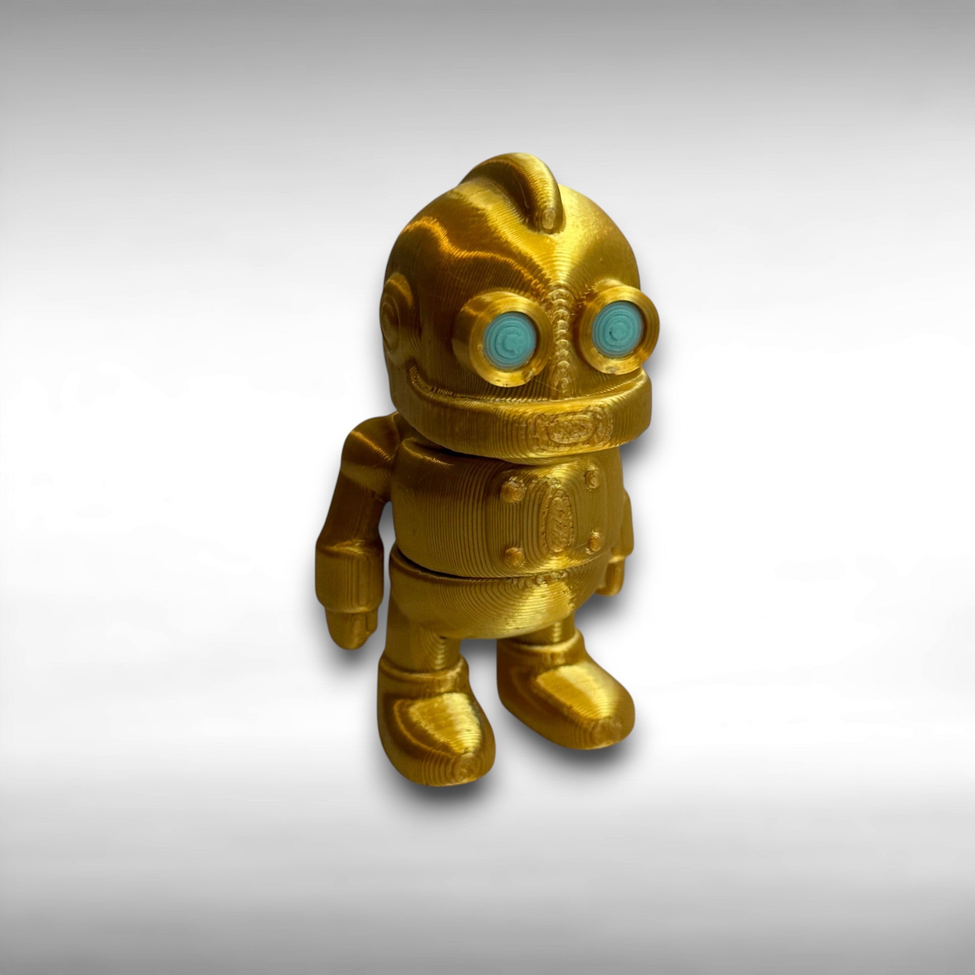Gold robot toy with turquoise eyes on a gray background