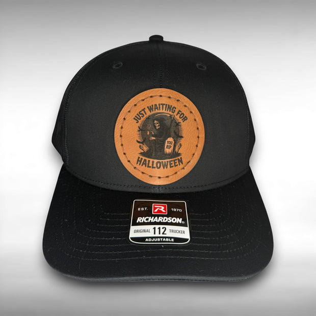 Black cap with a Richardson sticker and a brown leather patch featuring a grim reaper design with the phrase "just waiting for Halloween" on a gray background.
