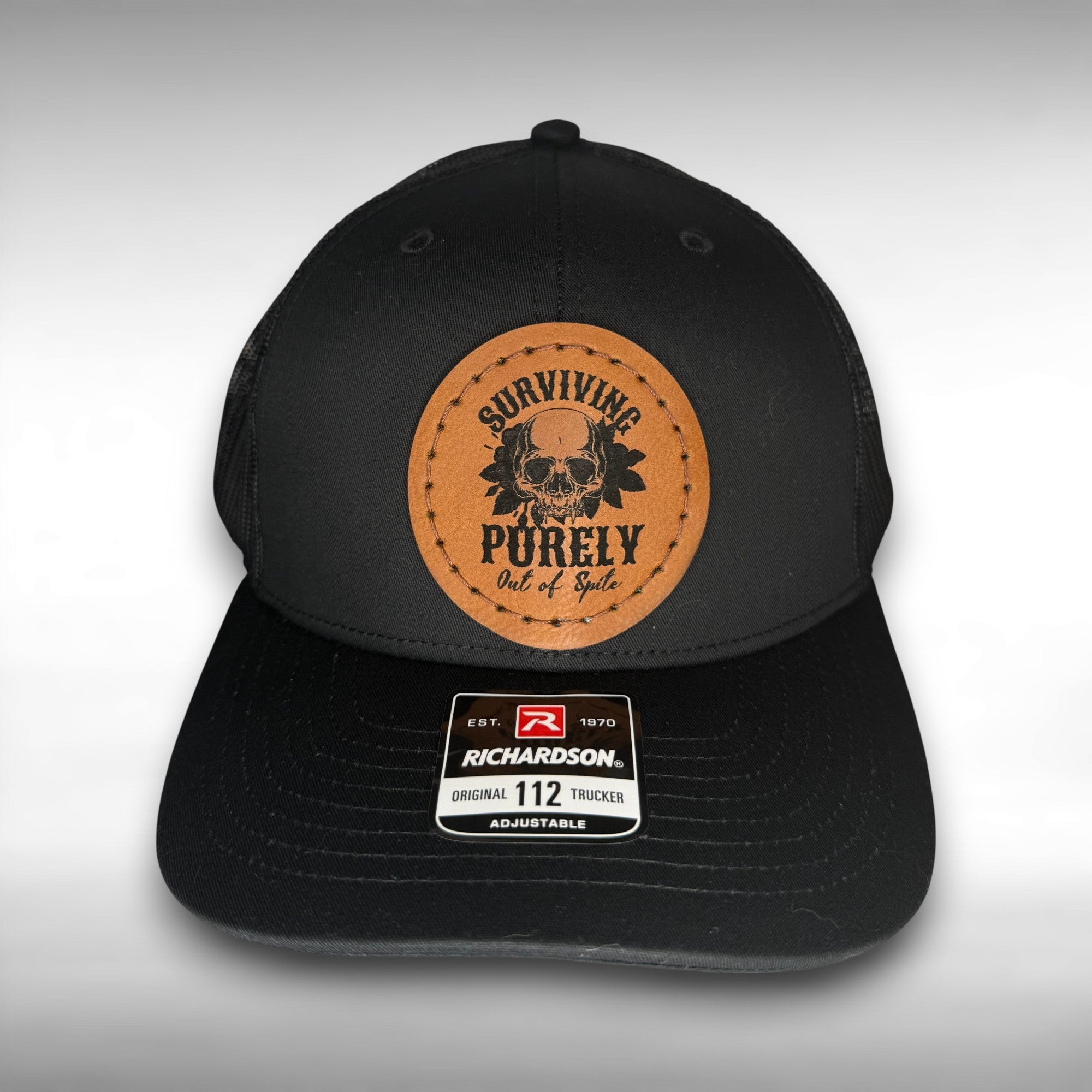 Black cap with a Richardson sticker and a brown leather patch featuring a skull and flowers design with the phrase 