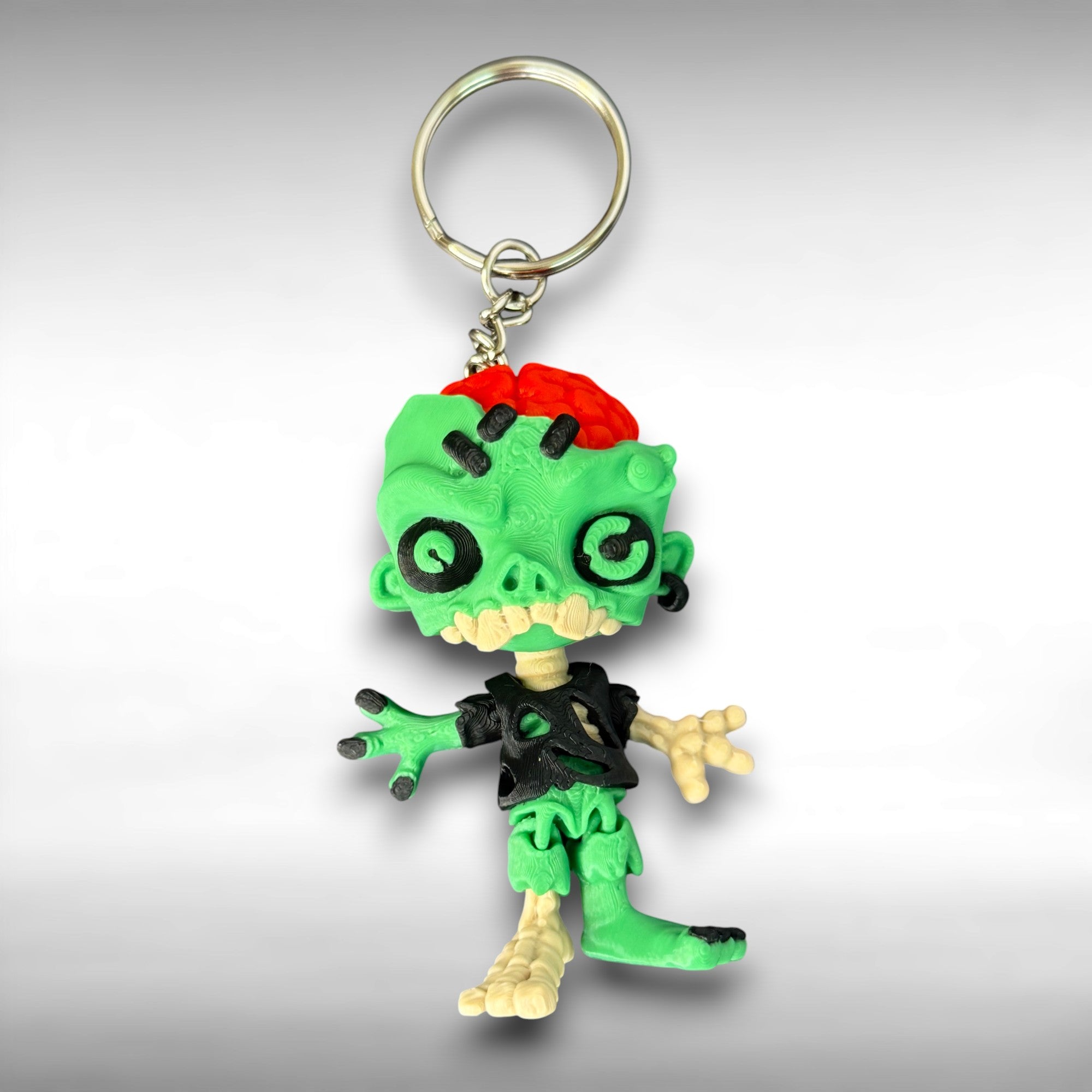 Zombie keychain with green skin, black eyes, and red brain on a gray background