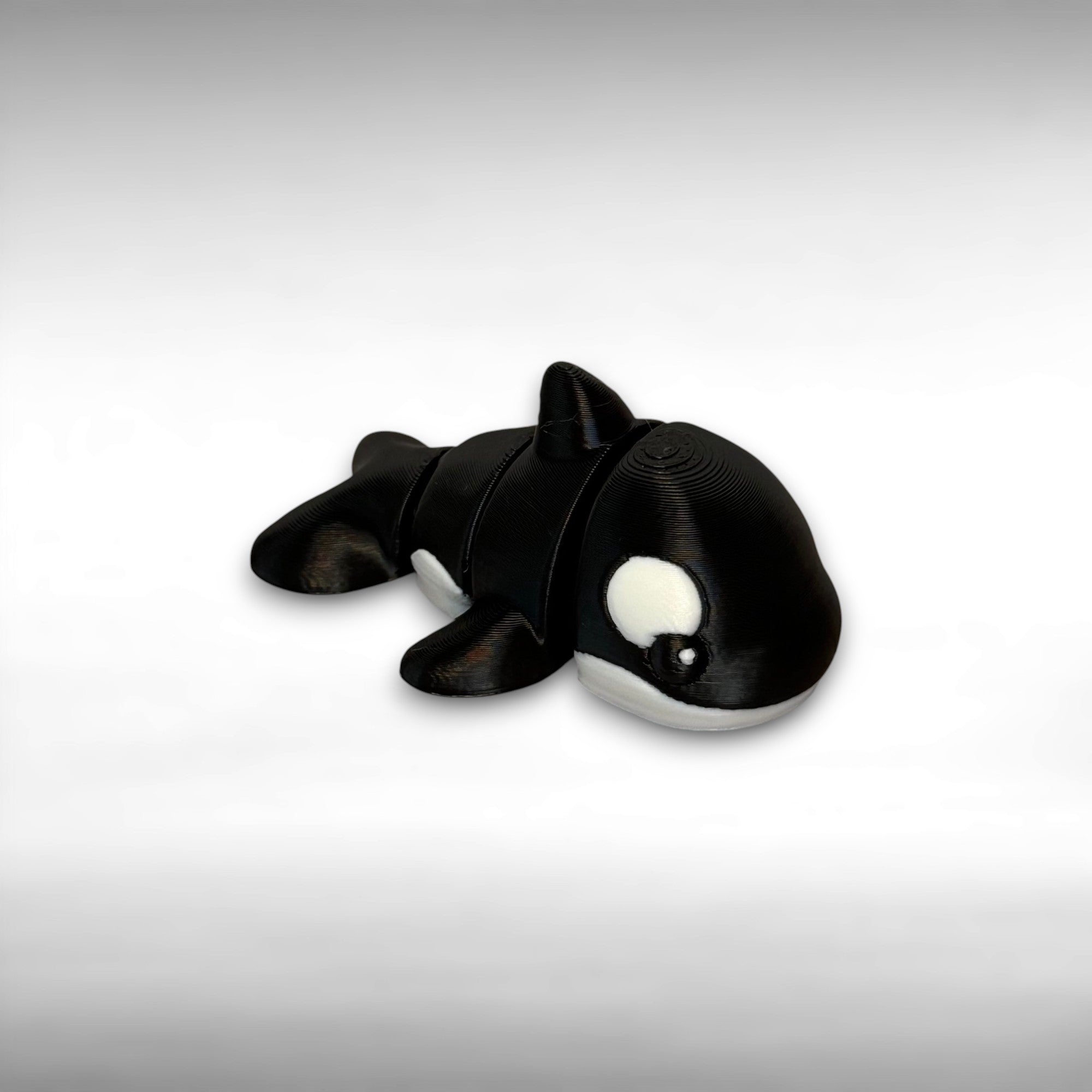 A small 3D printed orca toy with movable segments on a white background