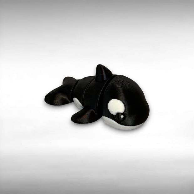 A small 3D printed orca toy with movable segments on a white background