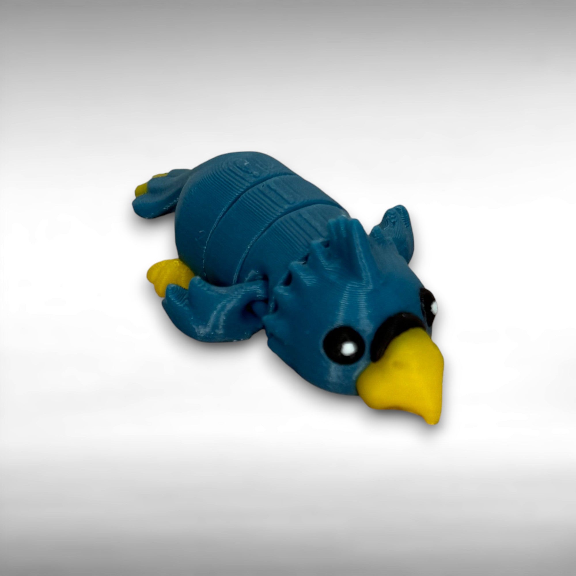 A small 3D printed blue and yellow articulated mini parrot toy on a white background
