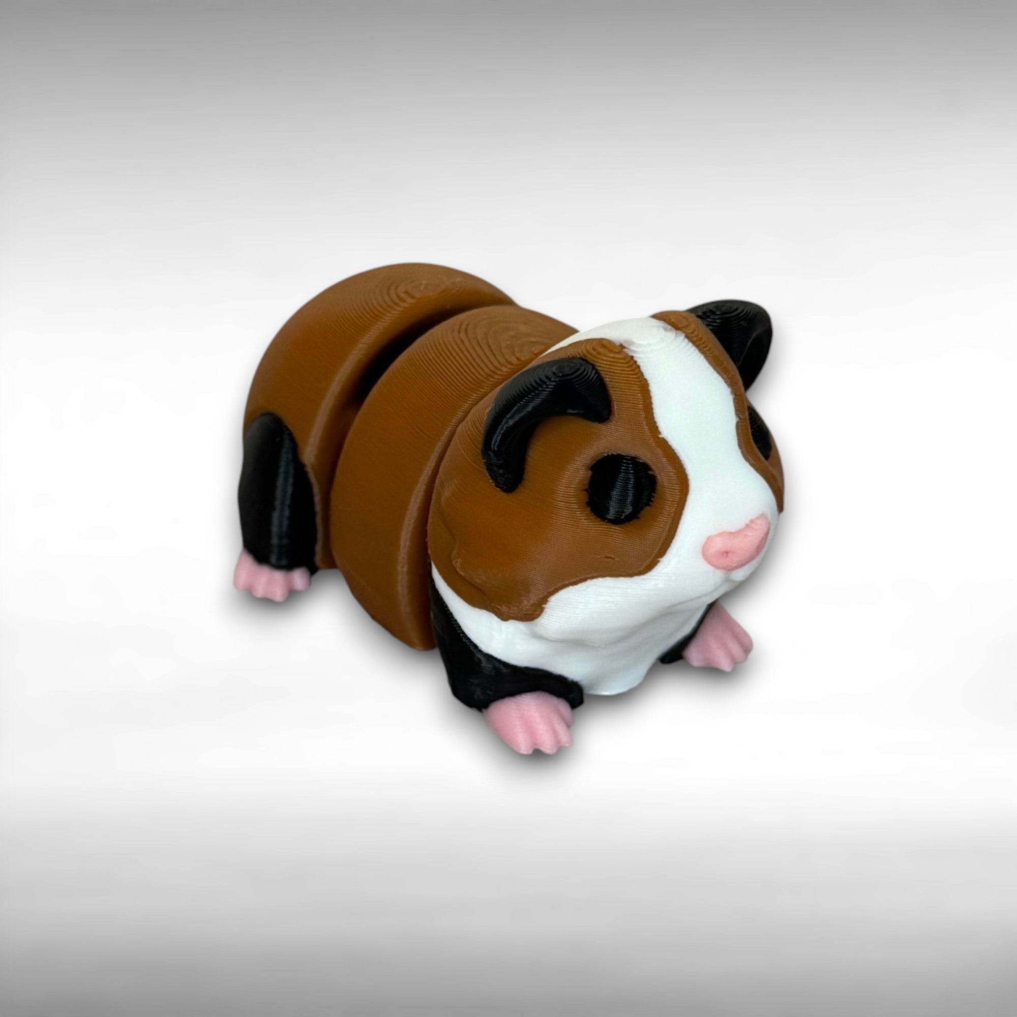 A small 3D printed brown, black, and white articulated mini guinea pig toy with pink nose and feet on a white background
