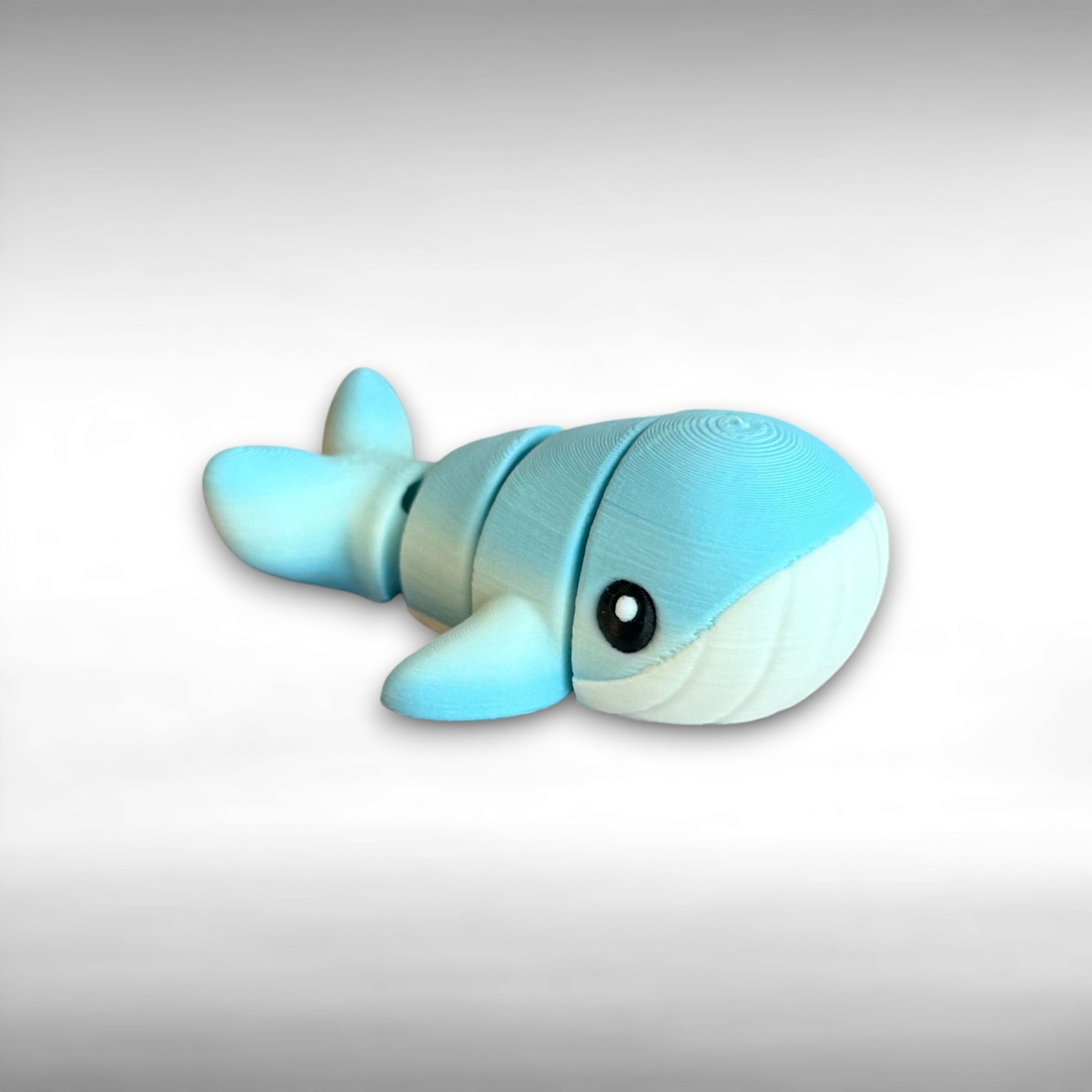 A small 3D printed articulated mini blue and white whale toy with articulated segments on a white background