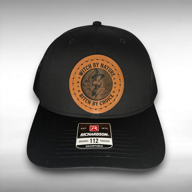 Black cap with a Richardson sticker and a brown leather patch featuring a witch and moon design with the phrase "witch by nature, bitch by choice" on a gray background