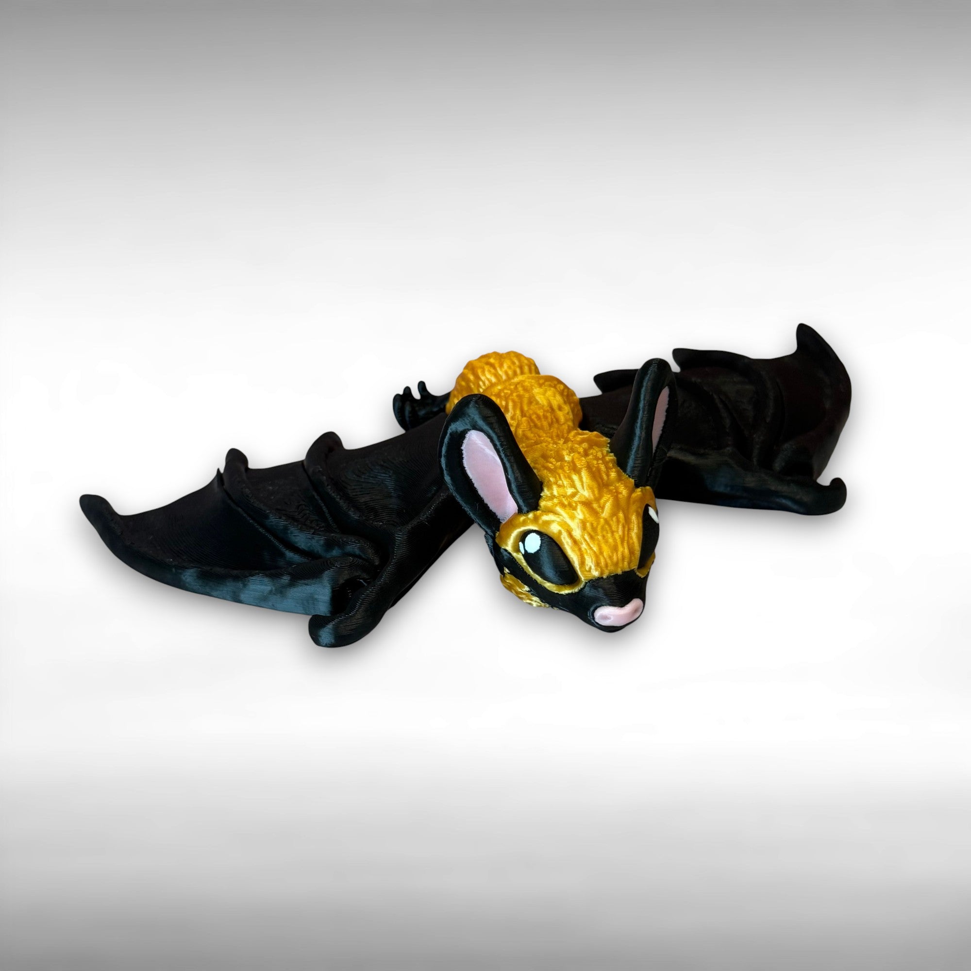 3D printed gold and black articulated bat against a gray background
