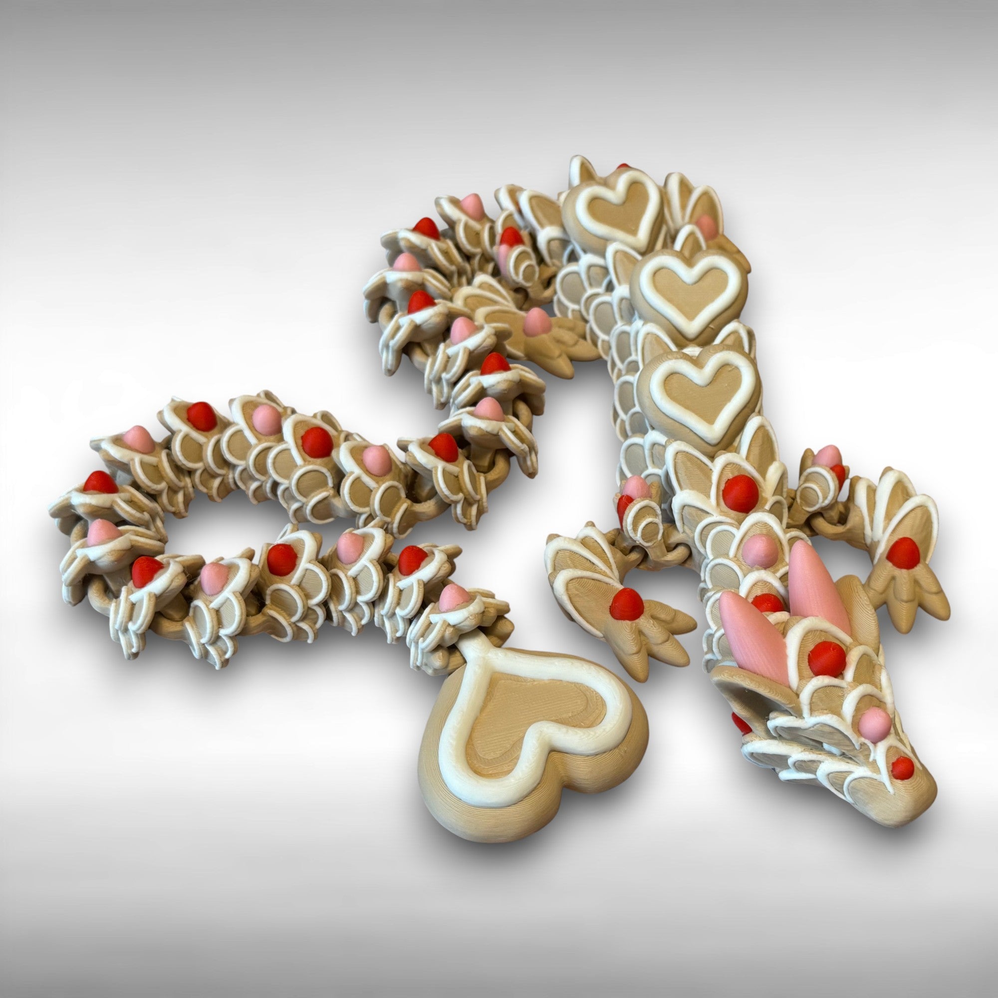 A beige colored 3D printed dragon figure with red, pink, and white heart-shaped cookie-like features against a gray background