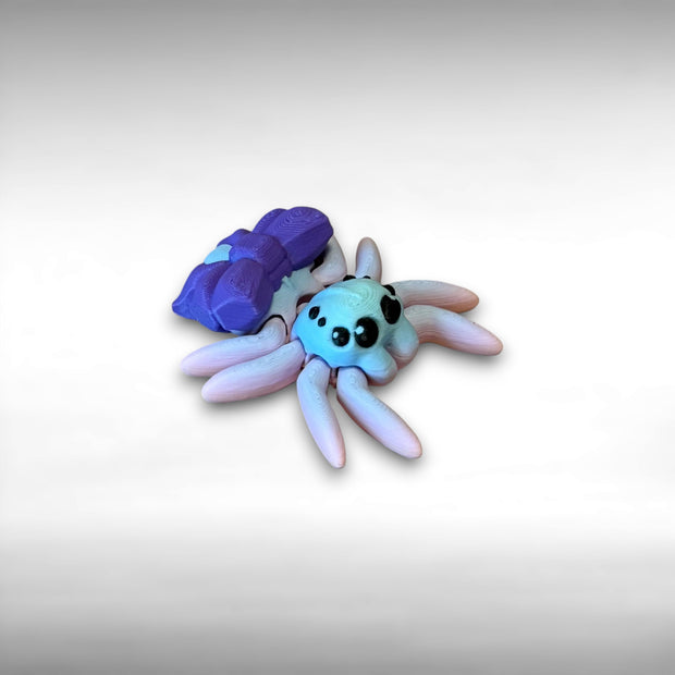 3D printed small spider with multicolor design and large purple bow against a white background