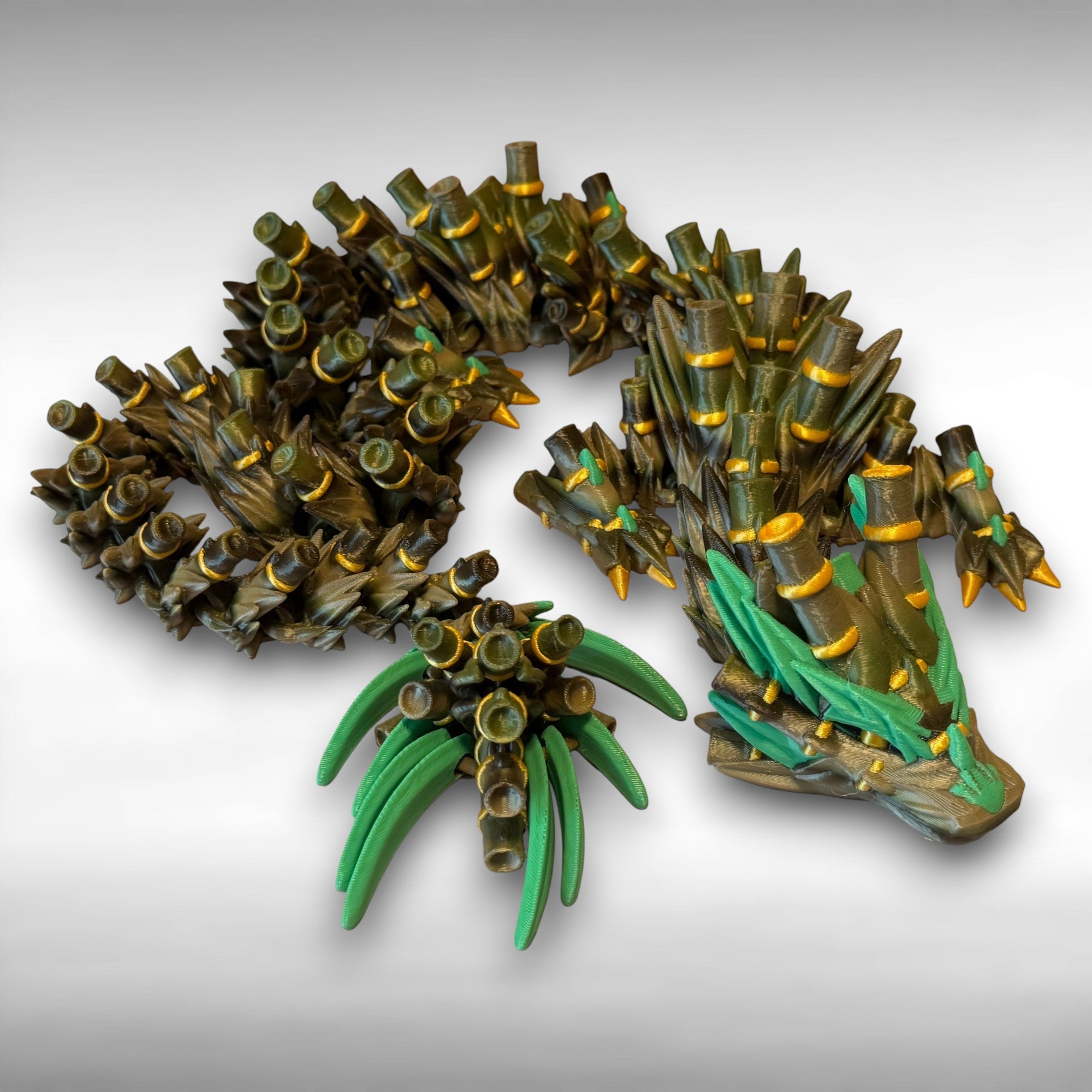 A green, brown, and gold colored 3D printed dragon figure with bamboo-like features against a gray background