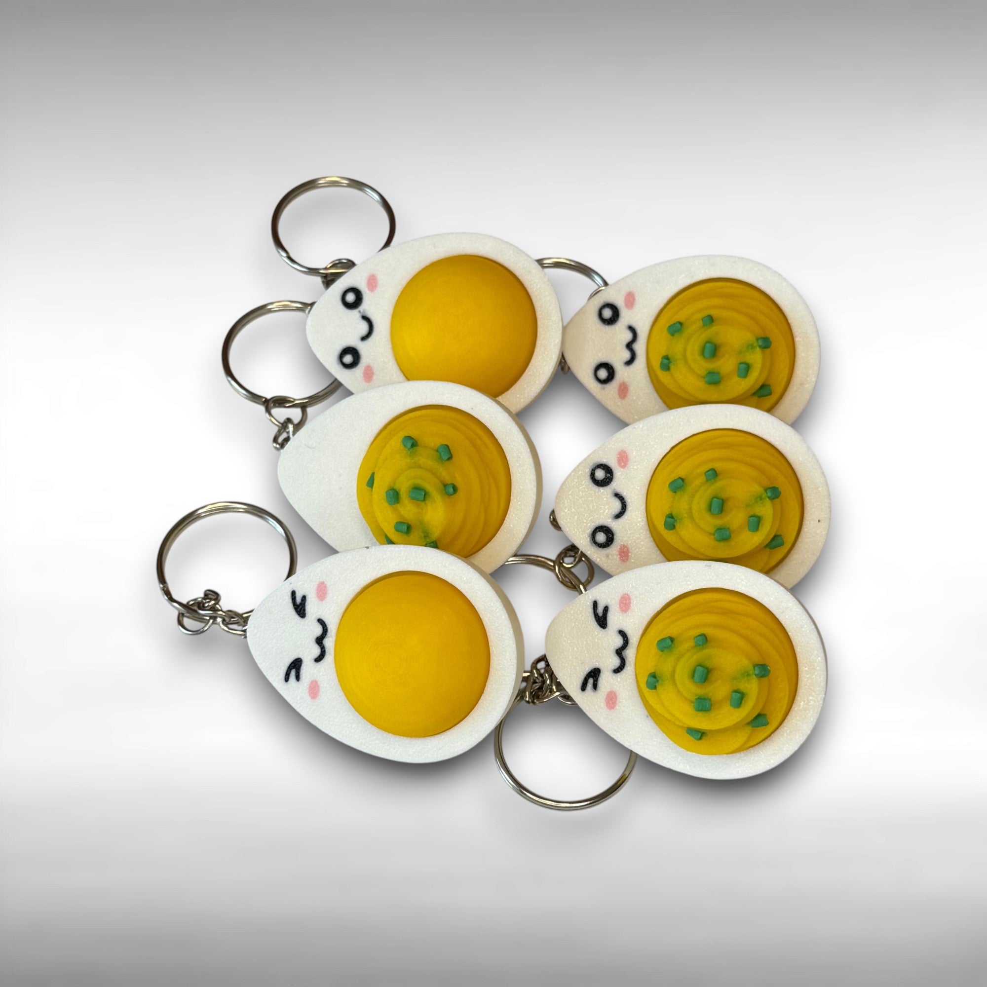 Set of hard-boiled egg and deviled egg keychains with cartoonish designs on a white background