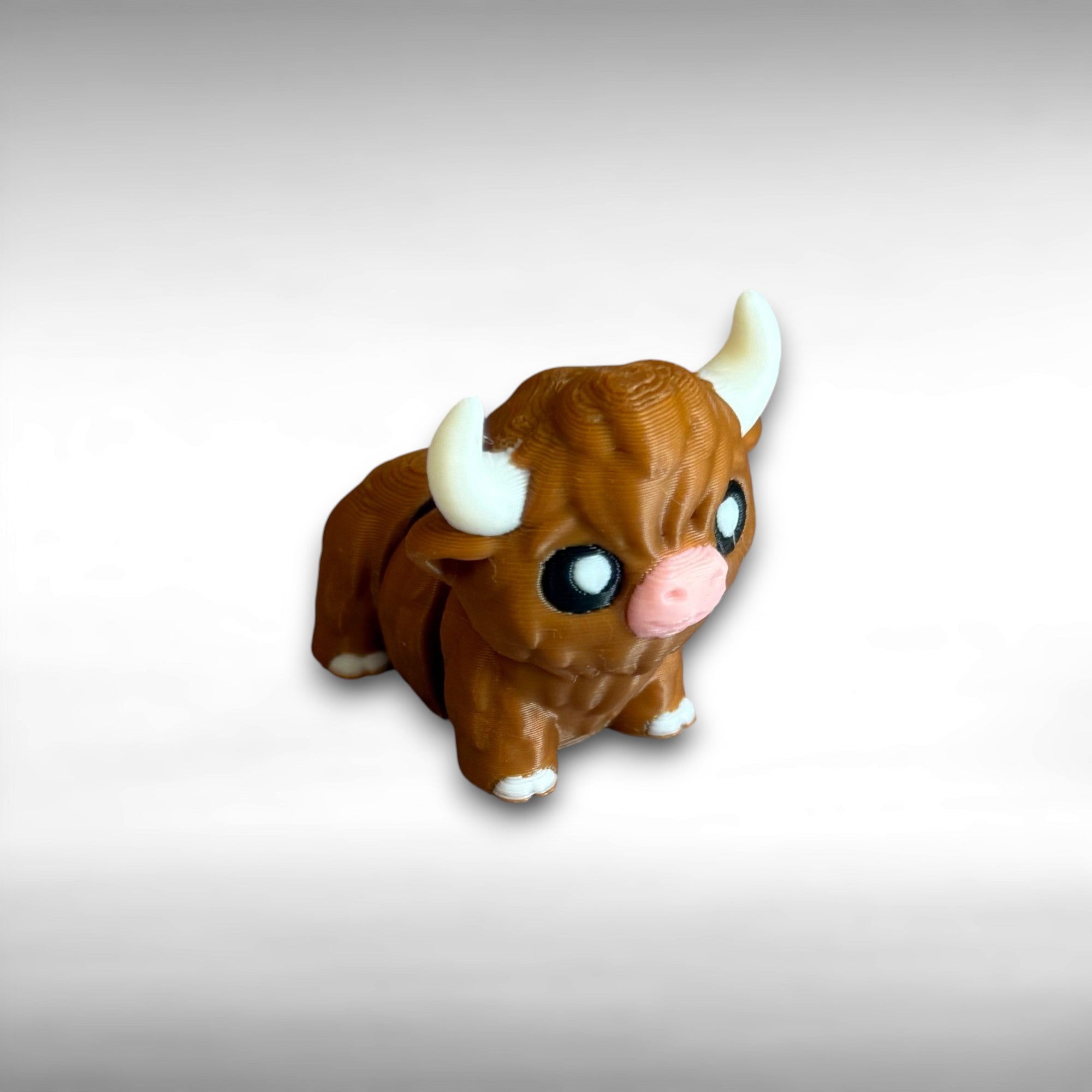A small 3D printed articulated brown Highland cow toy with movable joints, placed on a wooden surface.