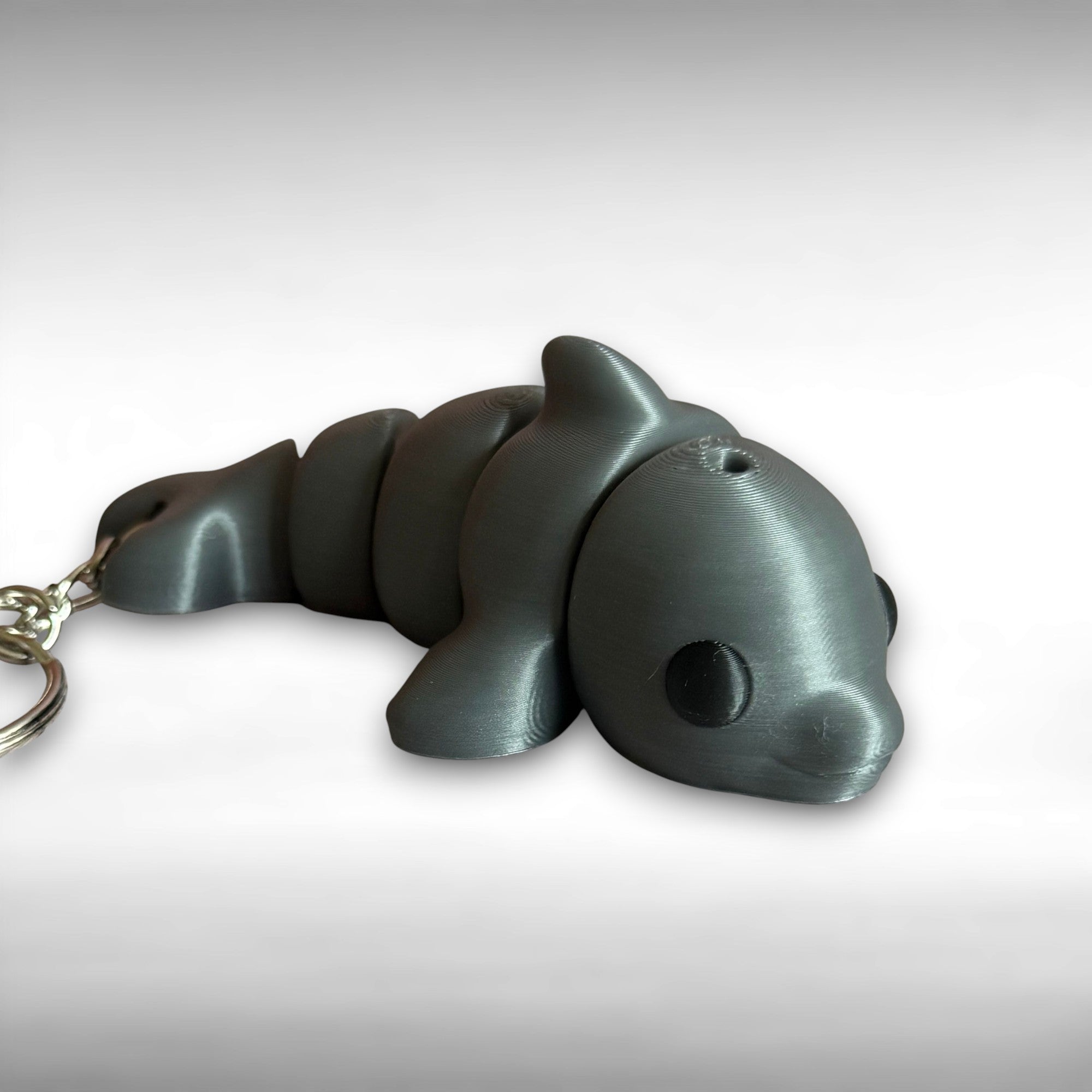 3D printed gray dolphin-shaped keychain on a light gray background
