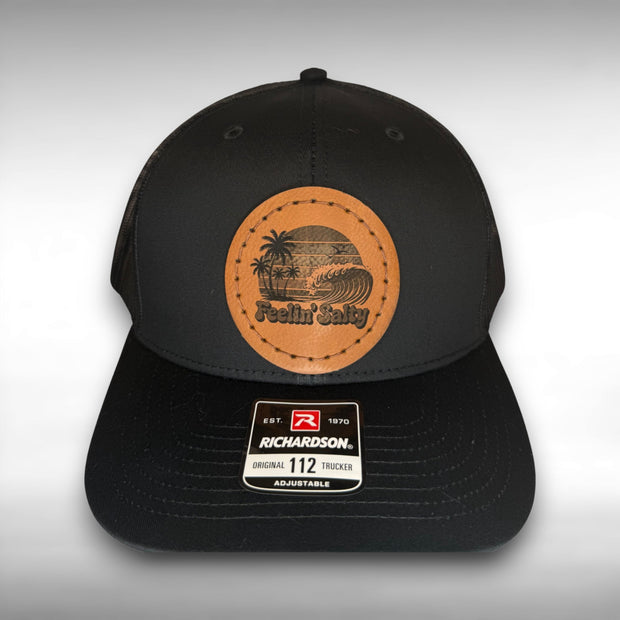 Black cap with a Richardson sticker and a brown leather patch featuring a palm tree and ocean wave design with the phrase "Feelin' Salty" on a gray background