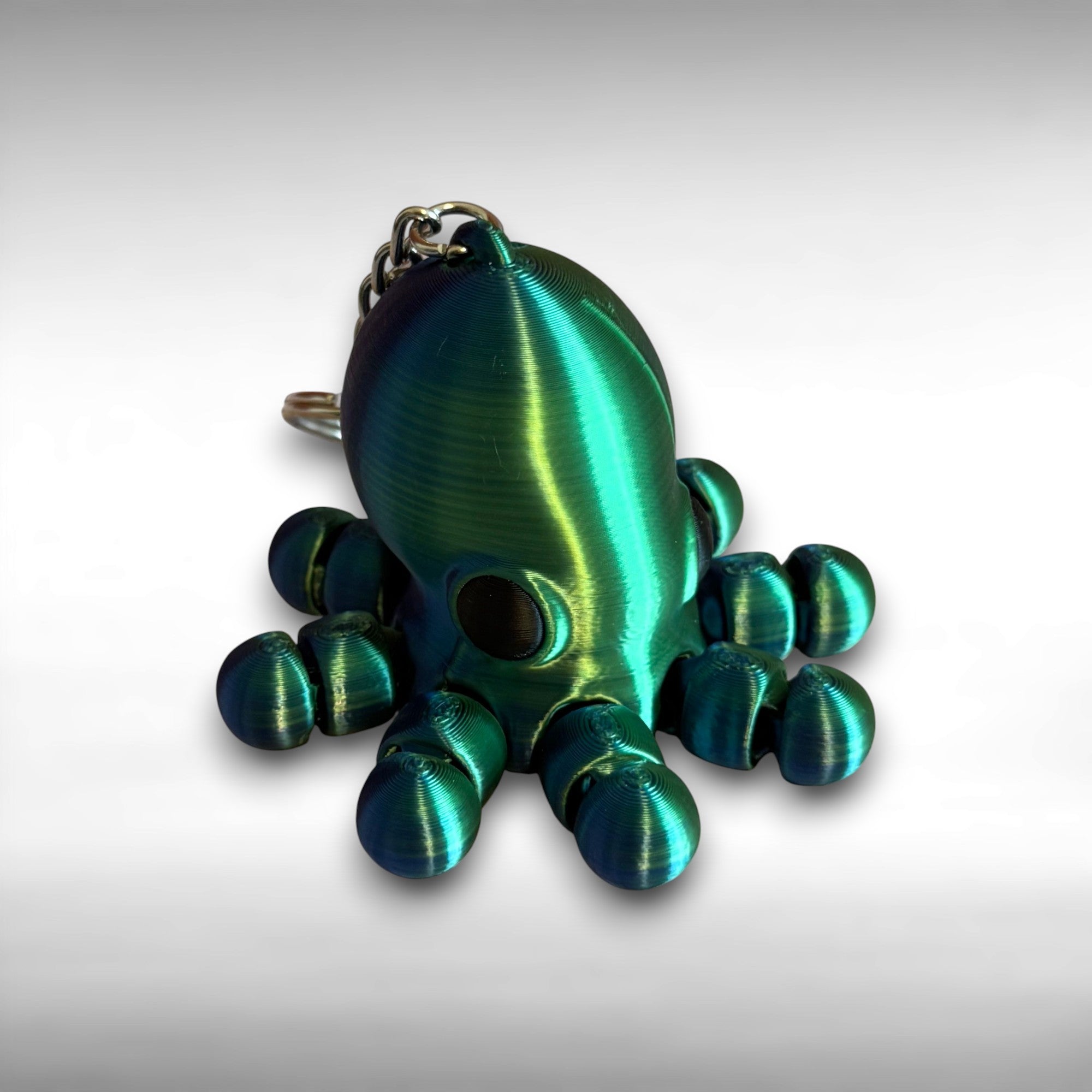 3D printed shiny green and blue octopus-shaped keychain on a light gray background