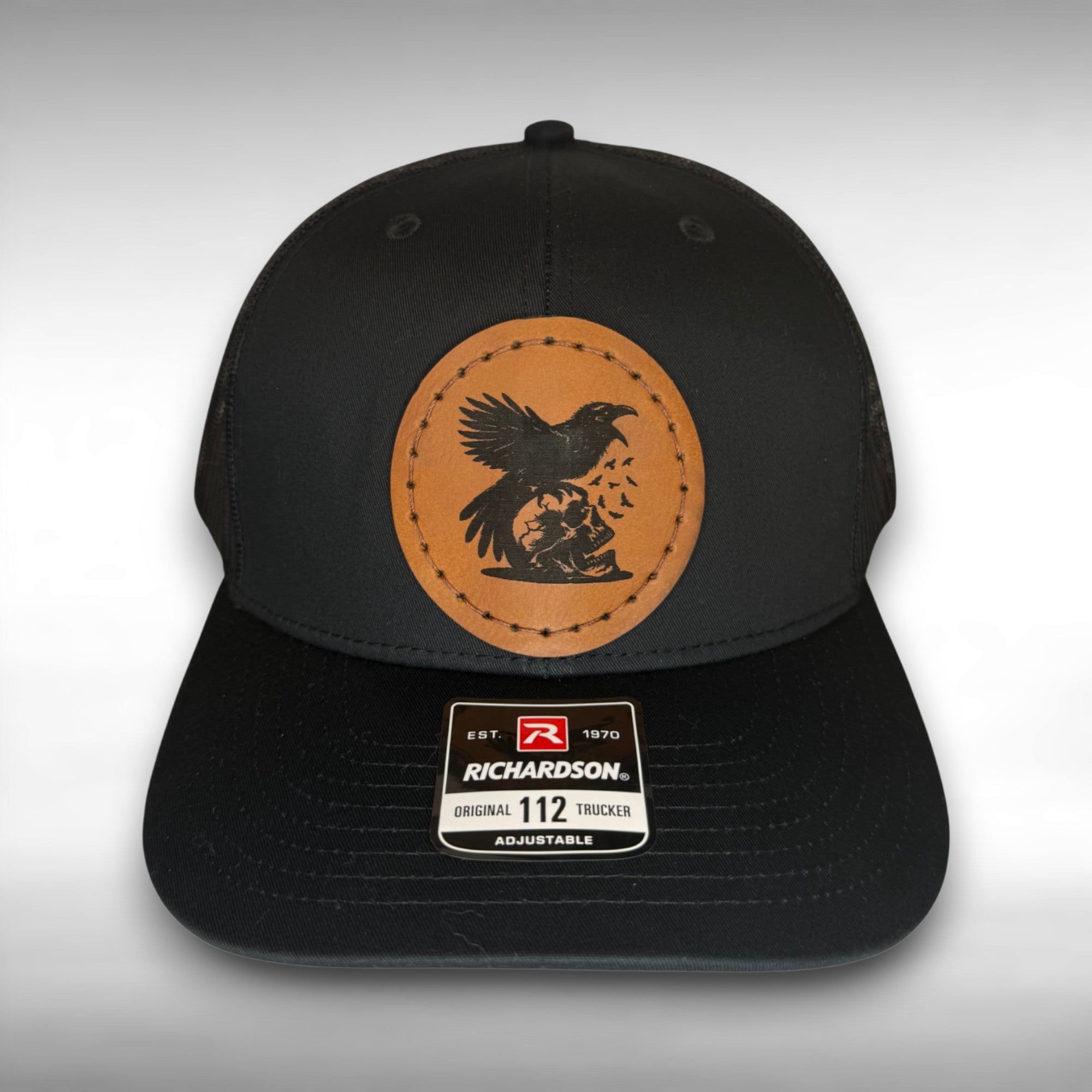 Black cap with a Richardson sticker and a brown leather patch featuring skull and raven design on a gray background