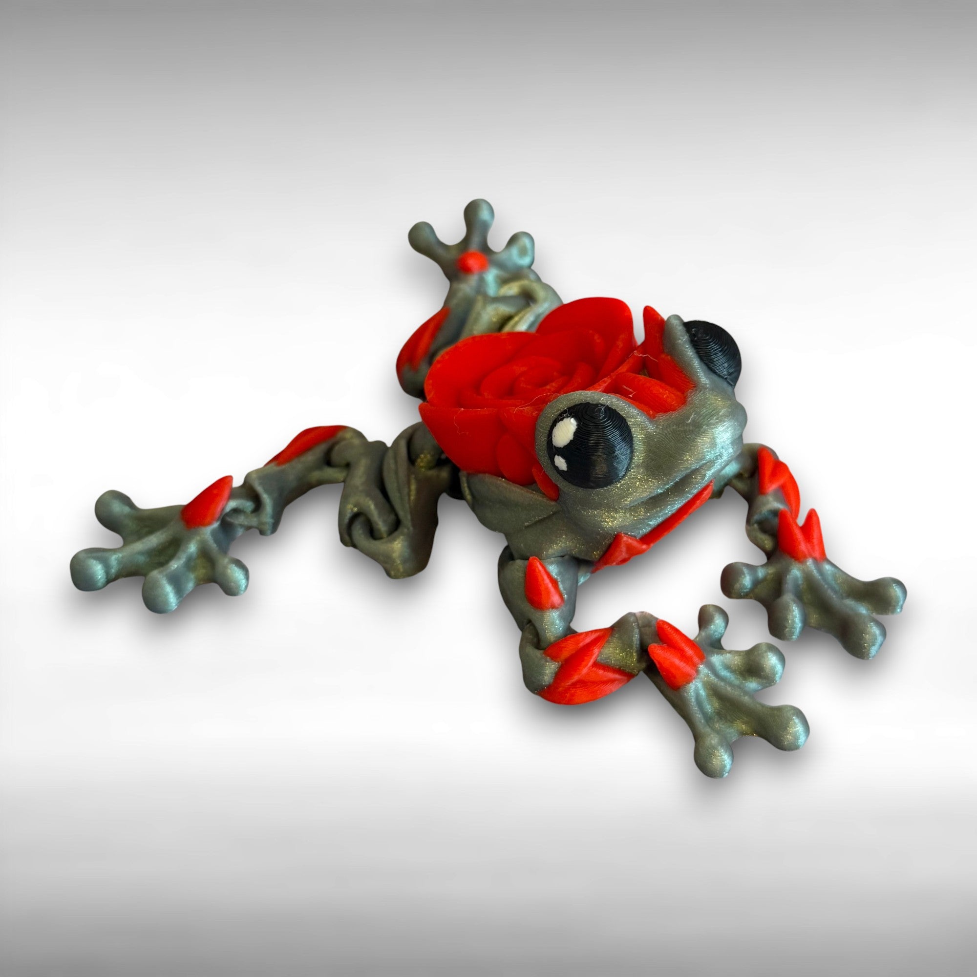 3D printed shimmer-green frog with red rose on it's back against a white background