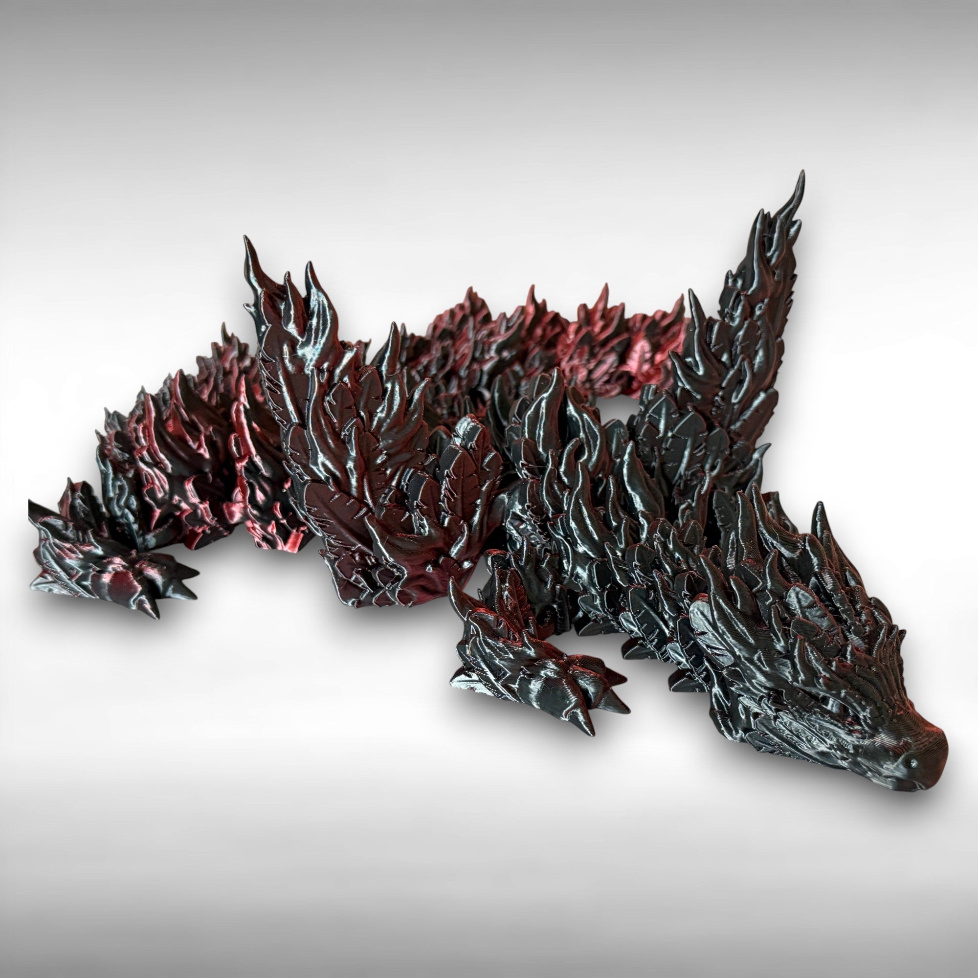 3D printed red and black dragon with flame-like features against a white background