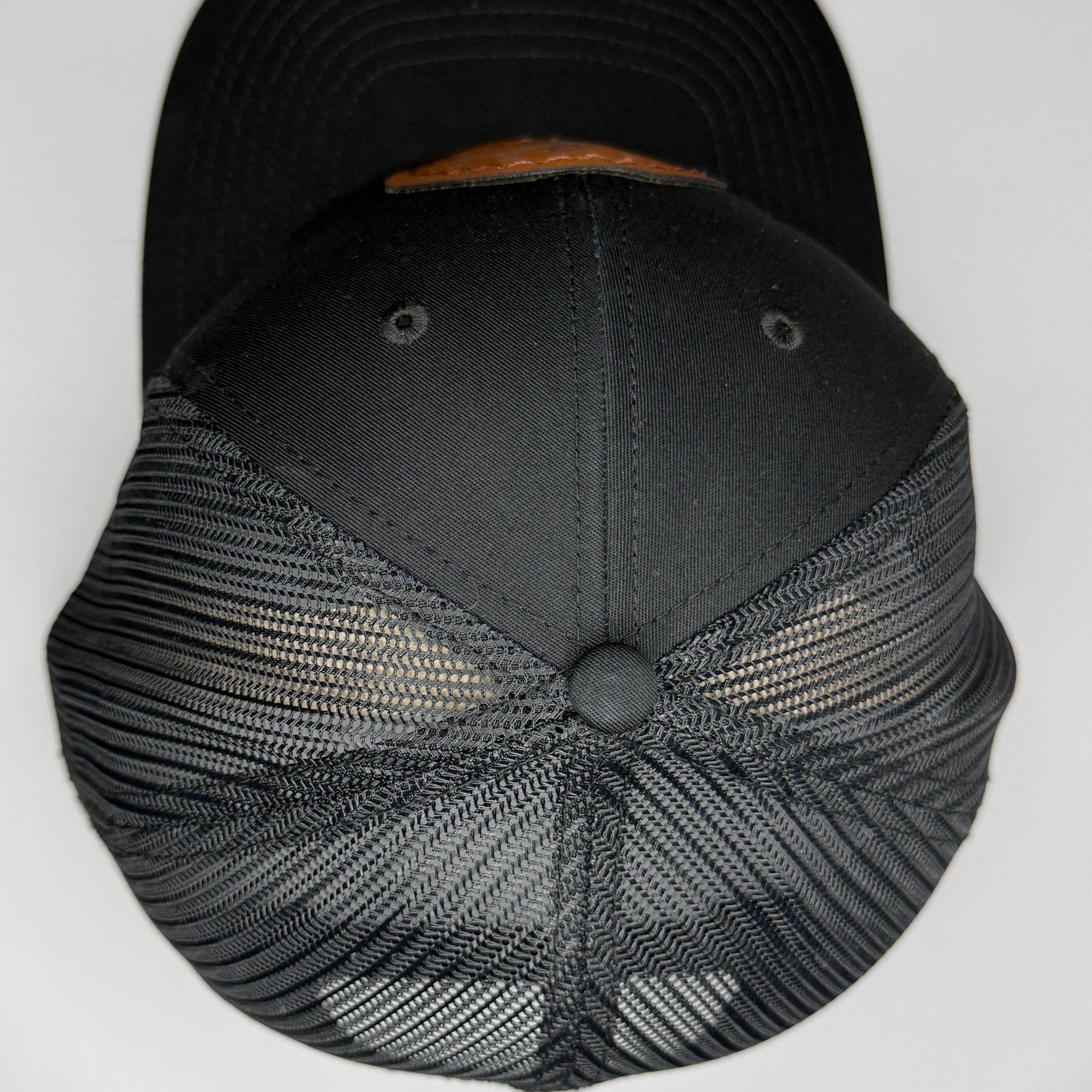 Top of a black cap with mesh back and a brown patch on a white background