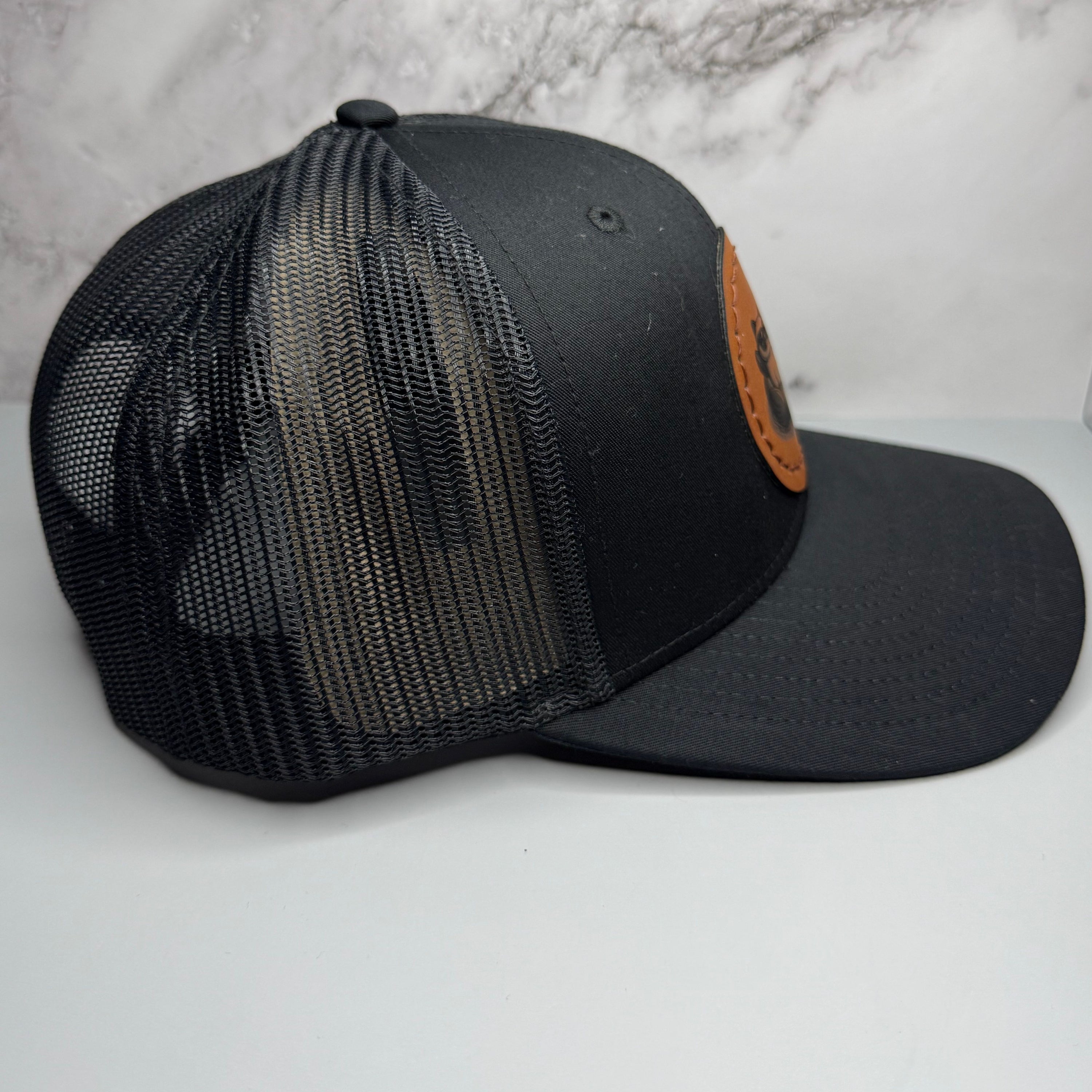 Black mesh cap with leather patch on a light gray background