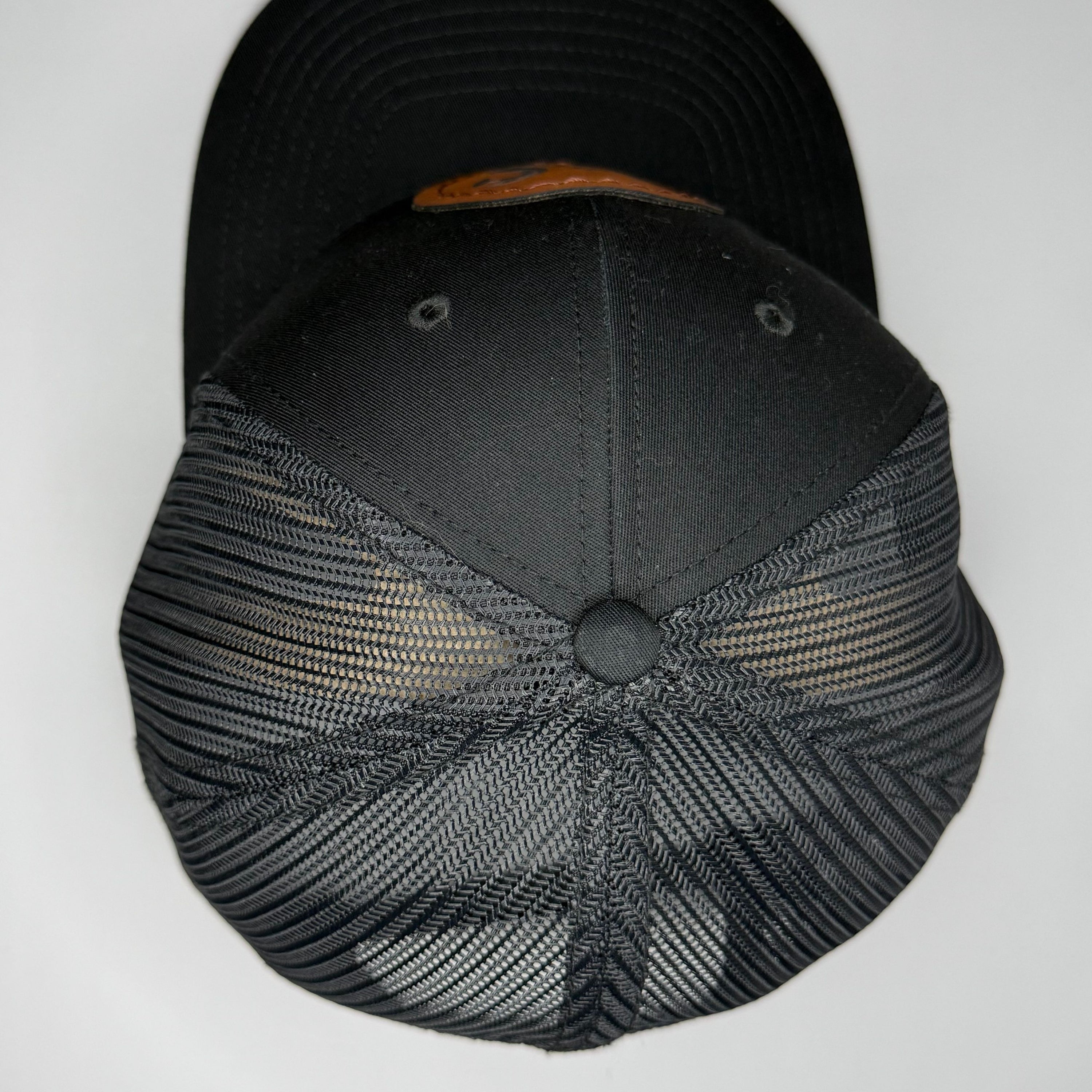 Top of a black cap with mesh back and brown patch on a white background