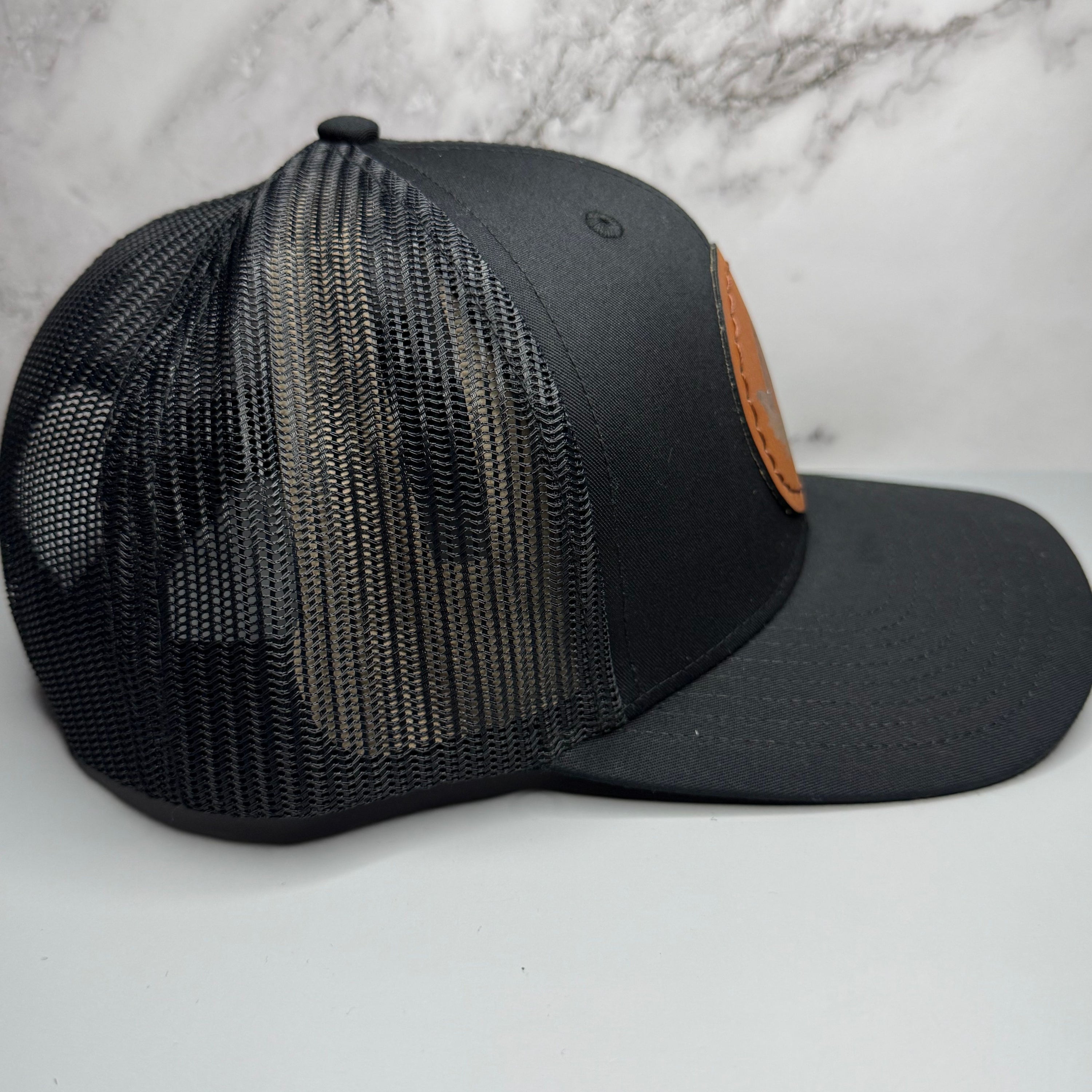 Black mesh cap with brown leather patch on a light gray background