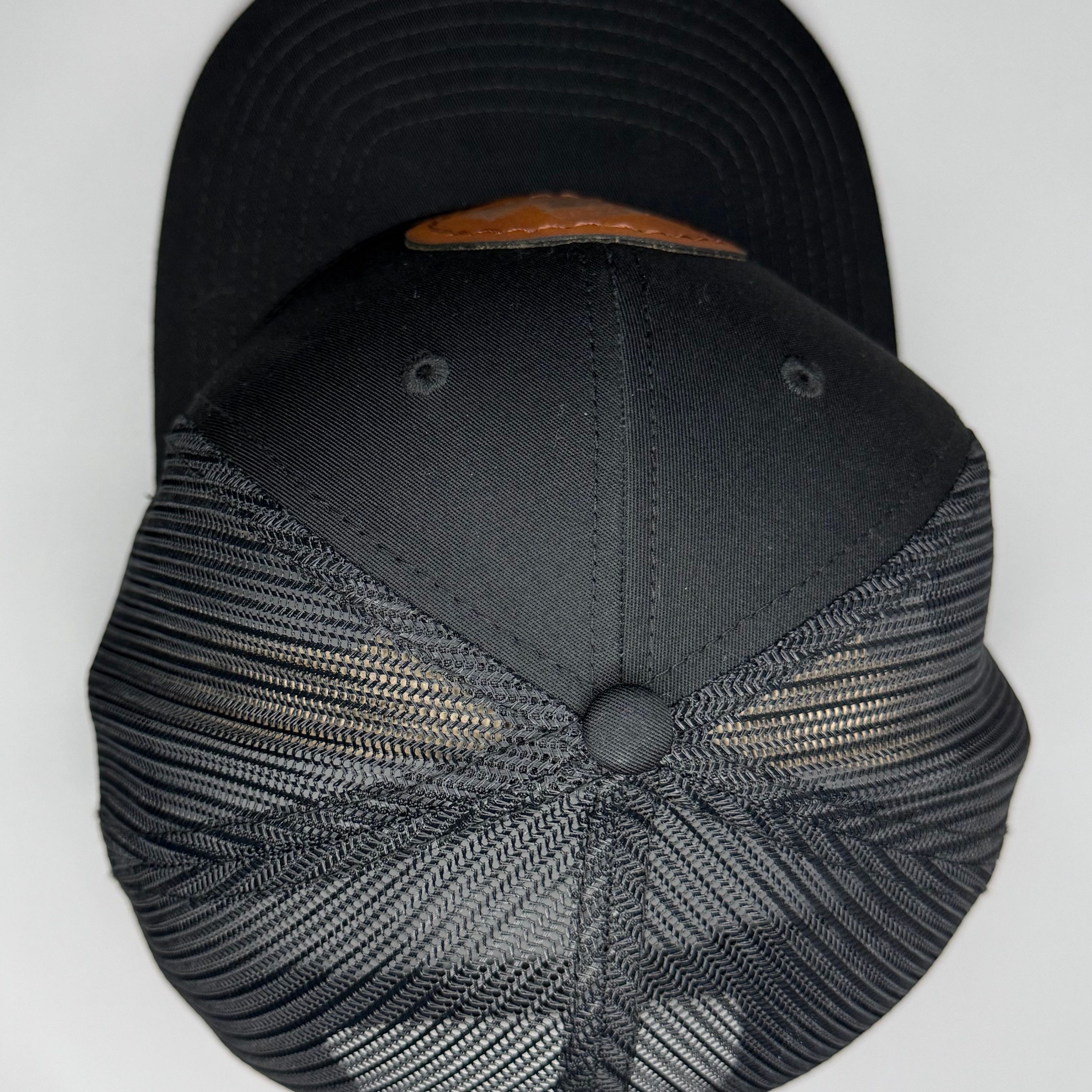 Top perspective of a black cap with mesh back and brown patch on a white background