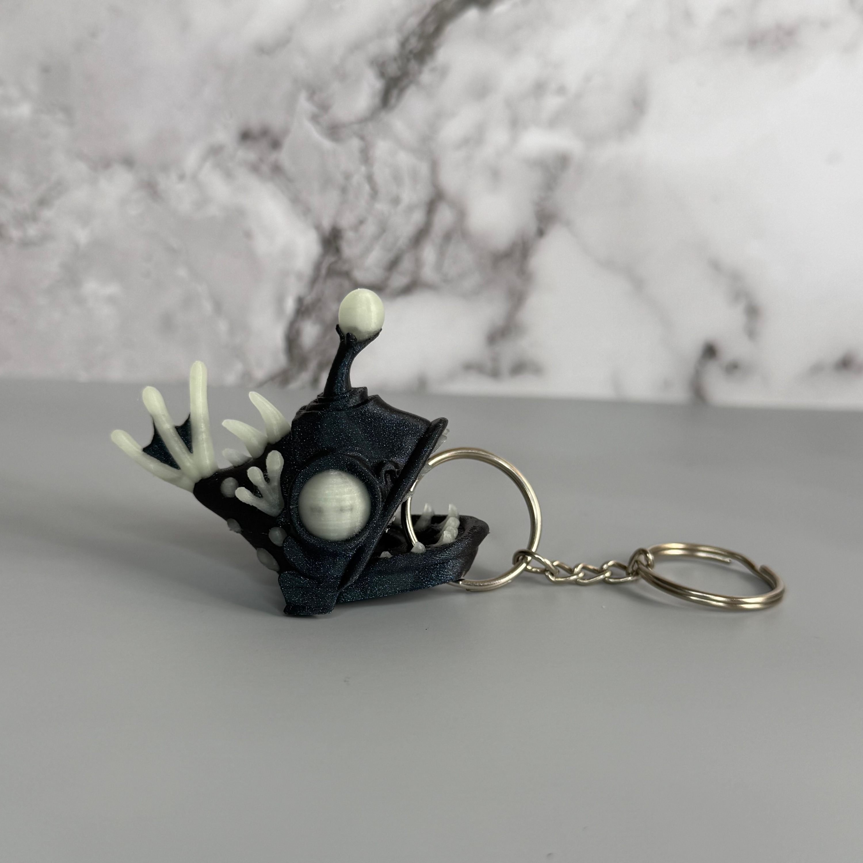 Sparkly blue angler fish keychain with white accents on a black and gray background
