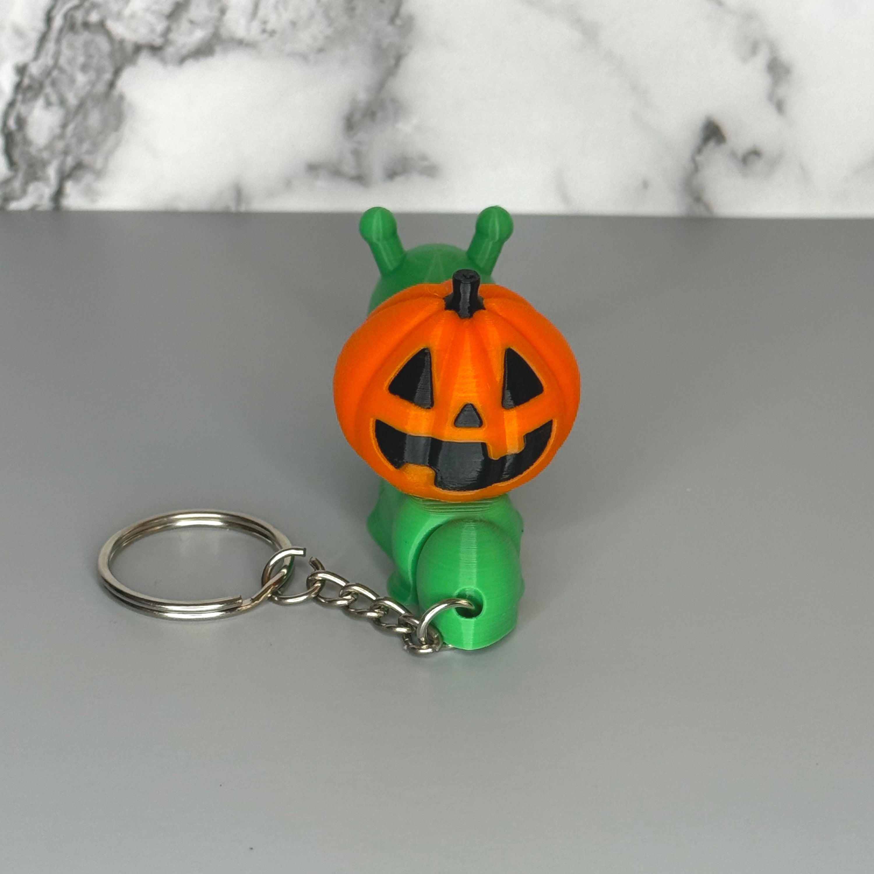 Back of green snail-shaped keychain with orange jack-o-lantern shell on a gray background.