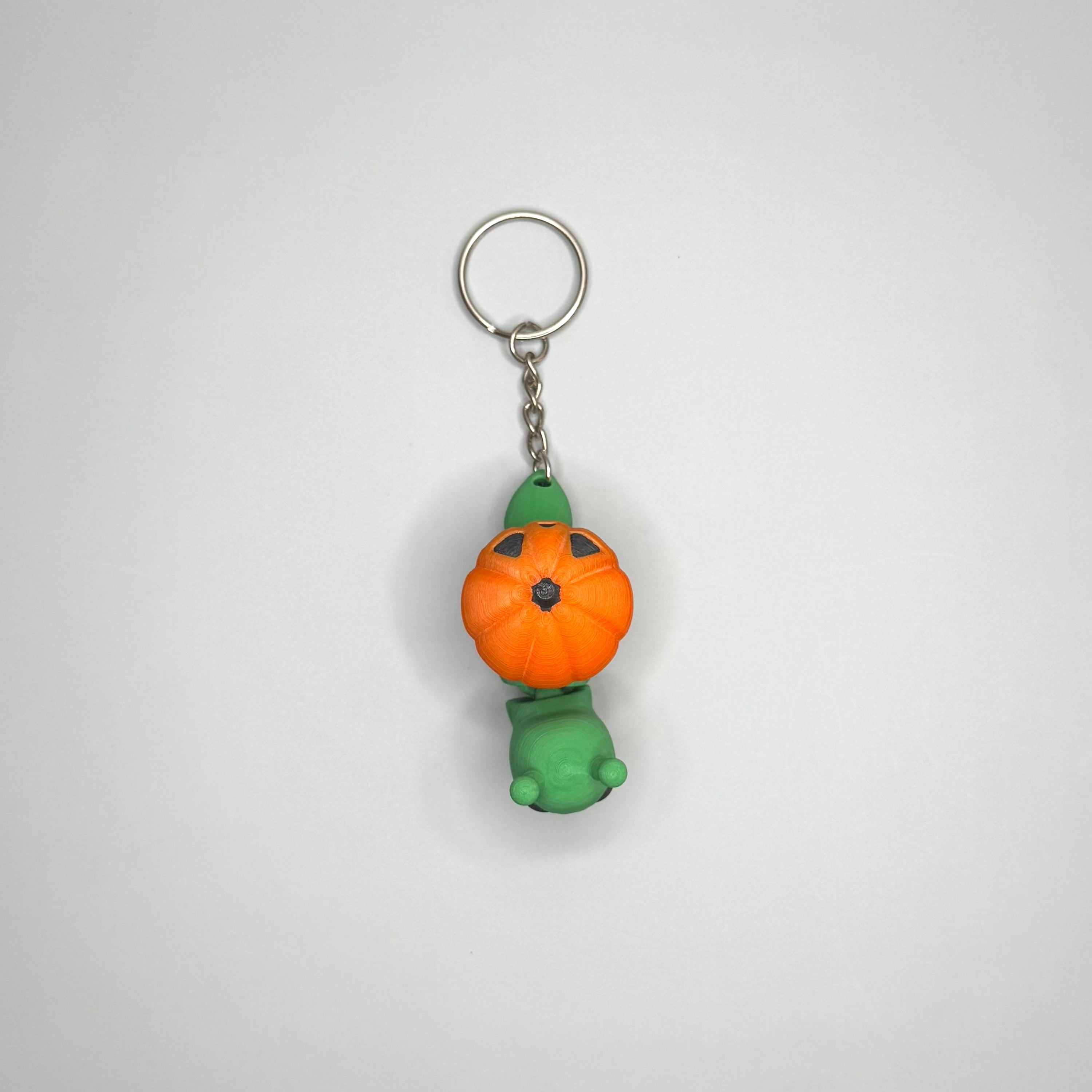 Top of green snail-shaped keychain with orange jack-o-lantern shell on a gray background.