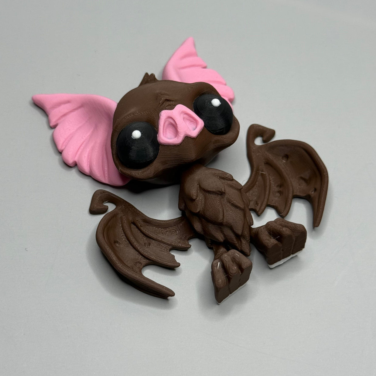 Toy figure of a brown bat with pink ears and nose on a gray background