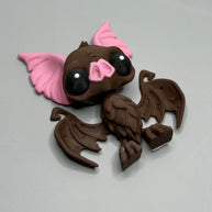 Toy figure of a brown bat with pink ears and nose on a gray background