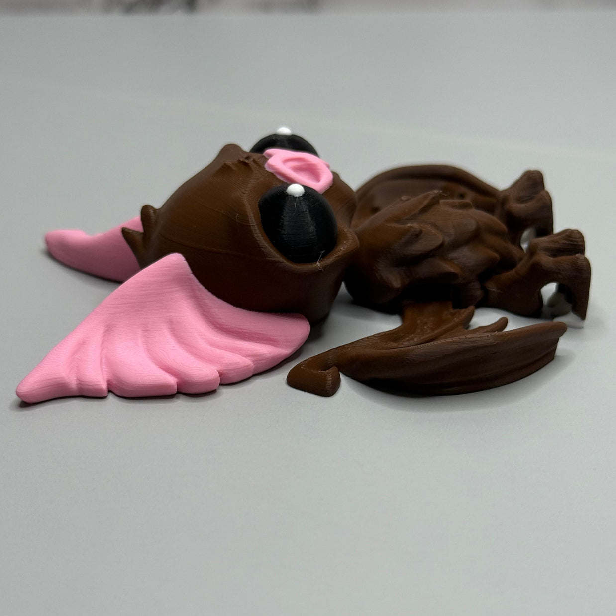 Left side of a figure of a brown bat with pink ears and nose on a gray background