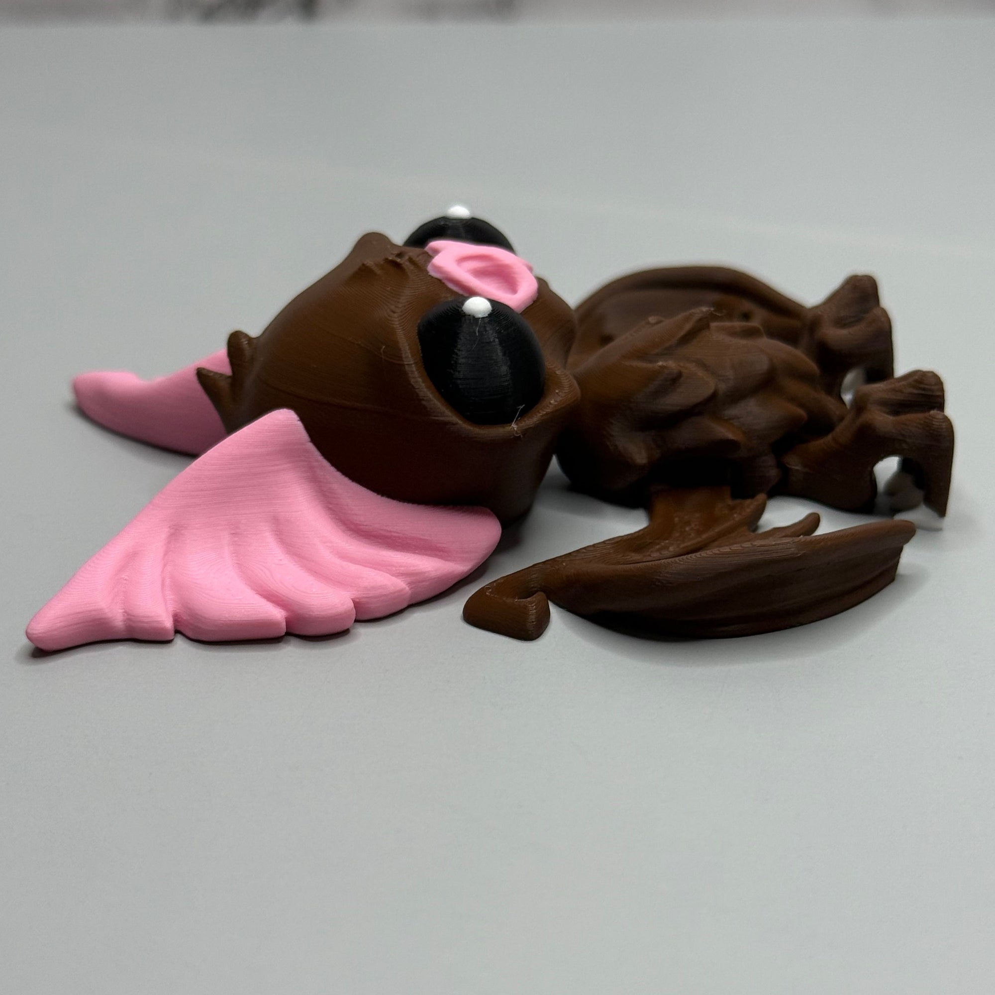 Left side of a figure of a brown bat with pink ears and nose on a gray background
